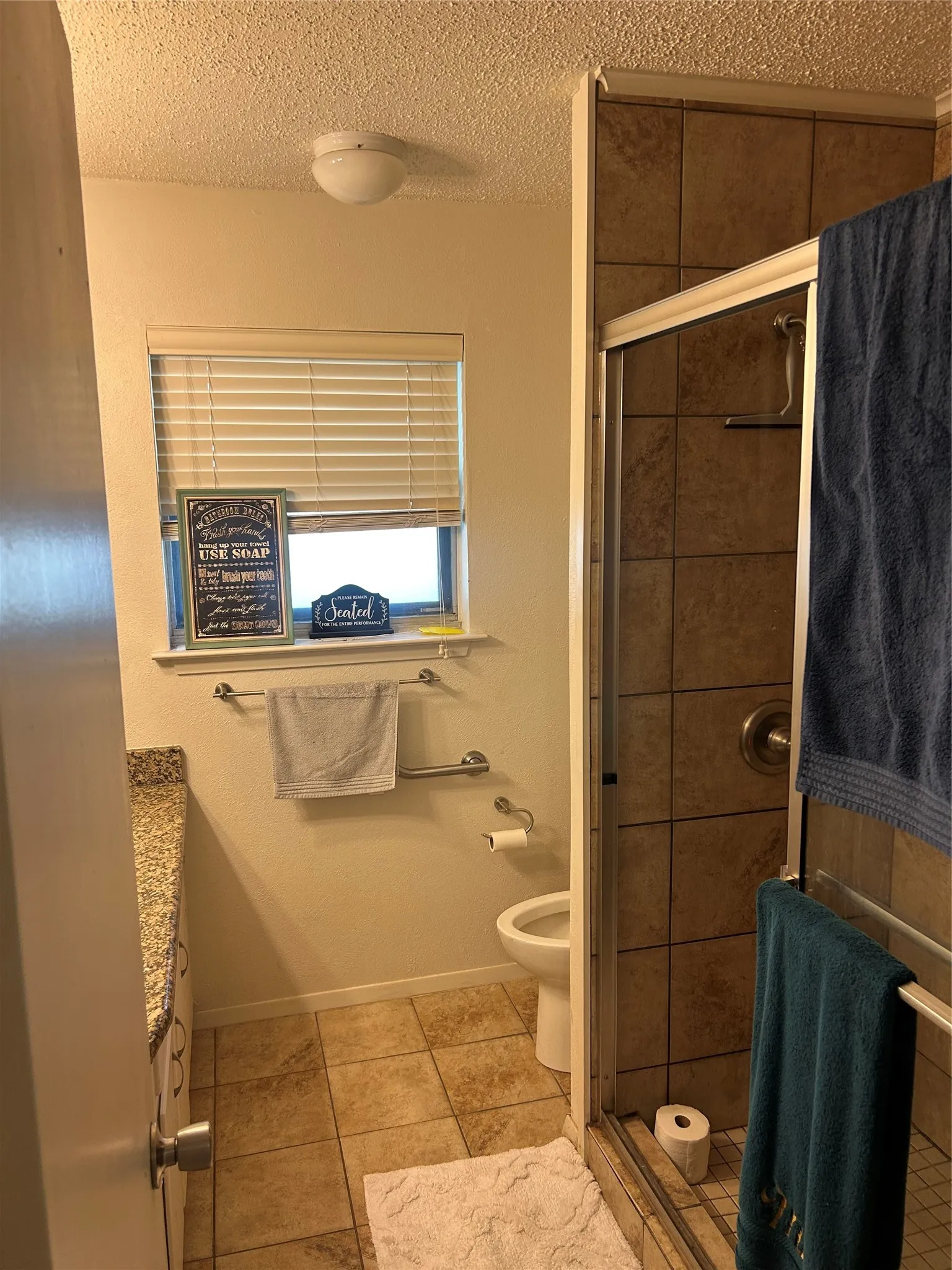Full bathroom featuring a stall shower, a textured ceiling, tile patterned floors, toilet, and baseboards