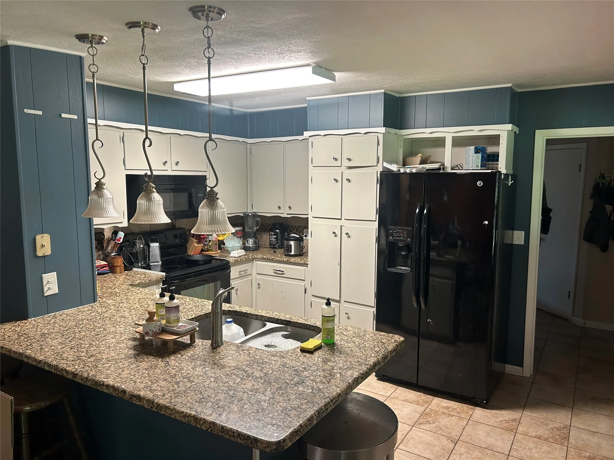 Kitchen featuring black appliances, a peninsula, light tile patterned floors, white cabinets, and a kitchen bar