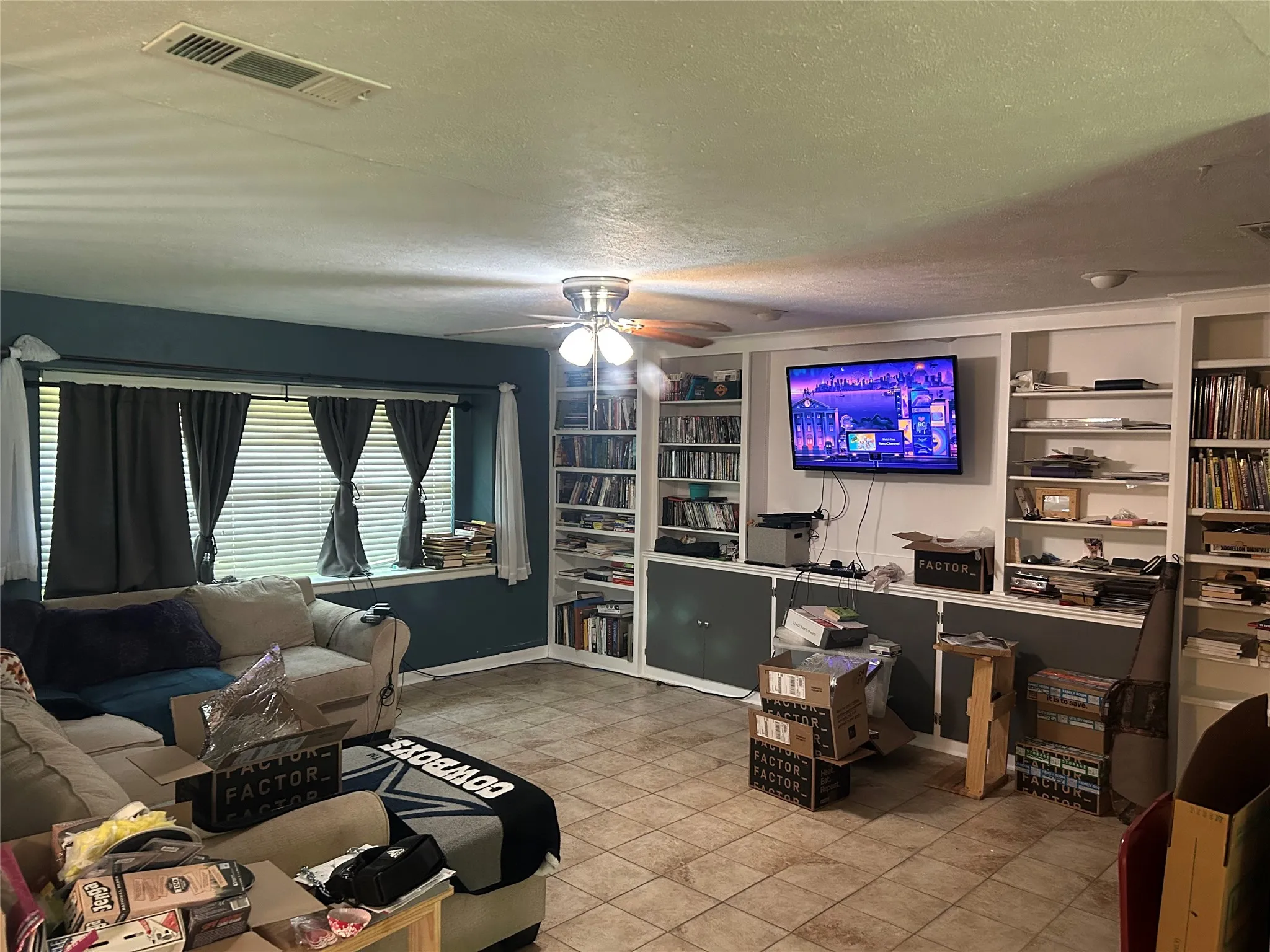 Tiled living area with a ceiling fan, a textured ceiling, built in features, and baseboards