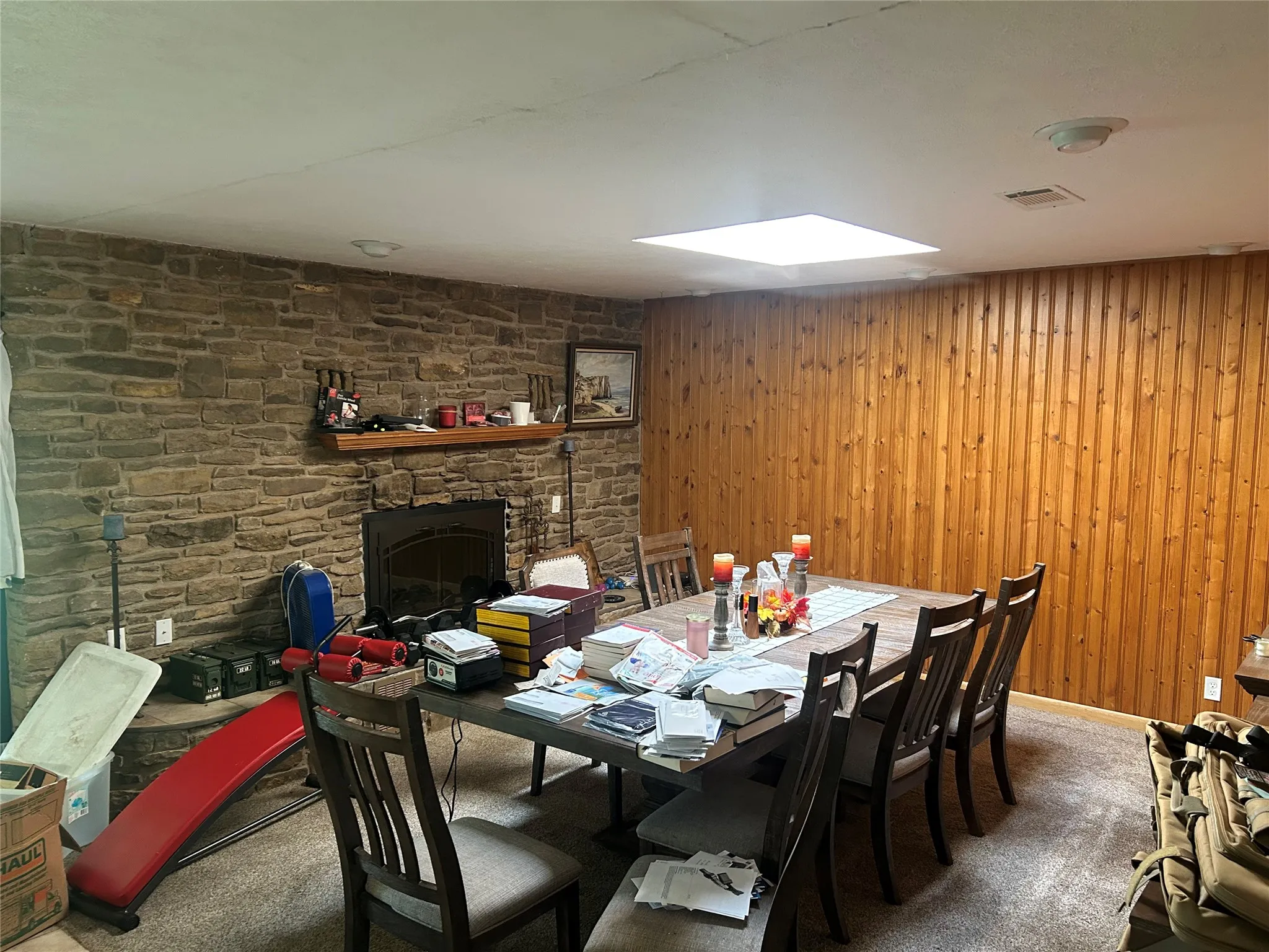 Dining area featuring carpet floors, wooden walls, sky light, and a stone fireplace