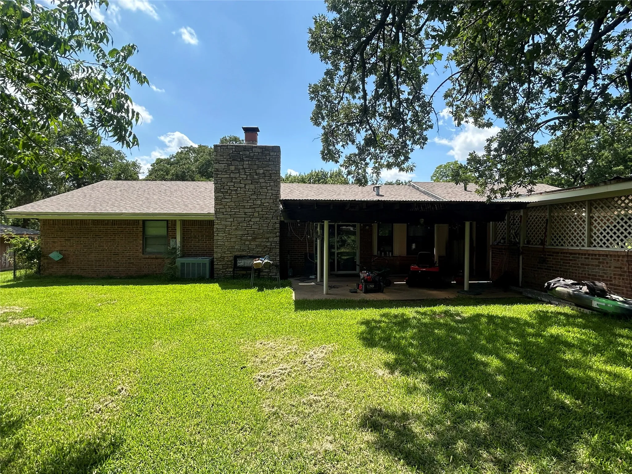 Back of property with cooling unit, a chimney, a patio area, and a lawn