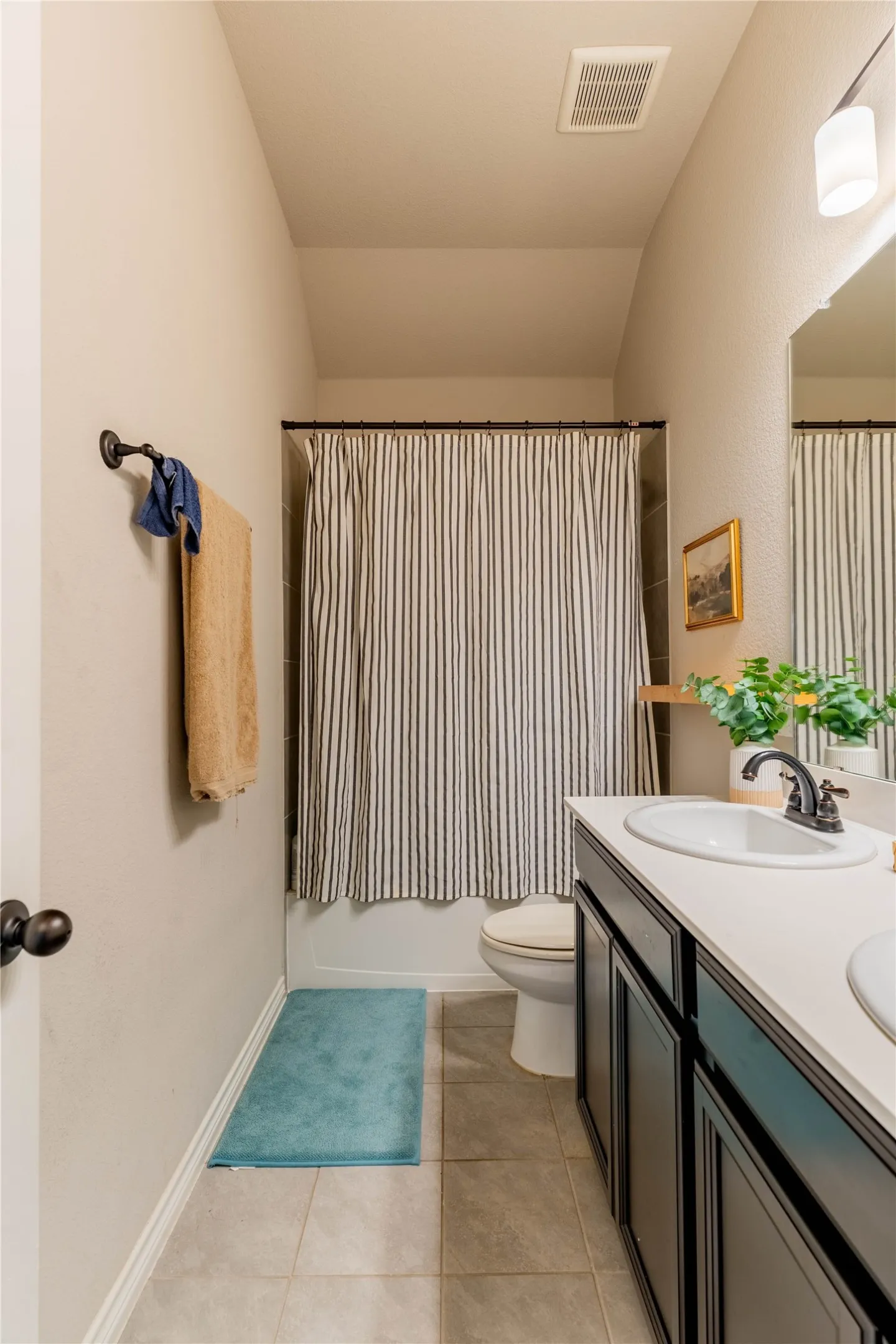 Full bathroom featuring double vanity, shower / bathtub combination with curtain, light tile patterned floors, and vaulted ceiling