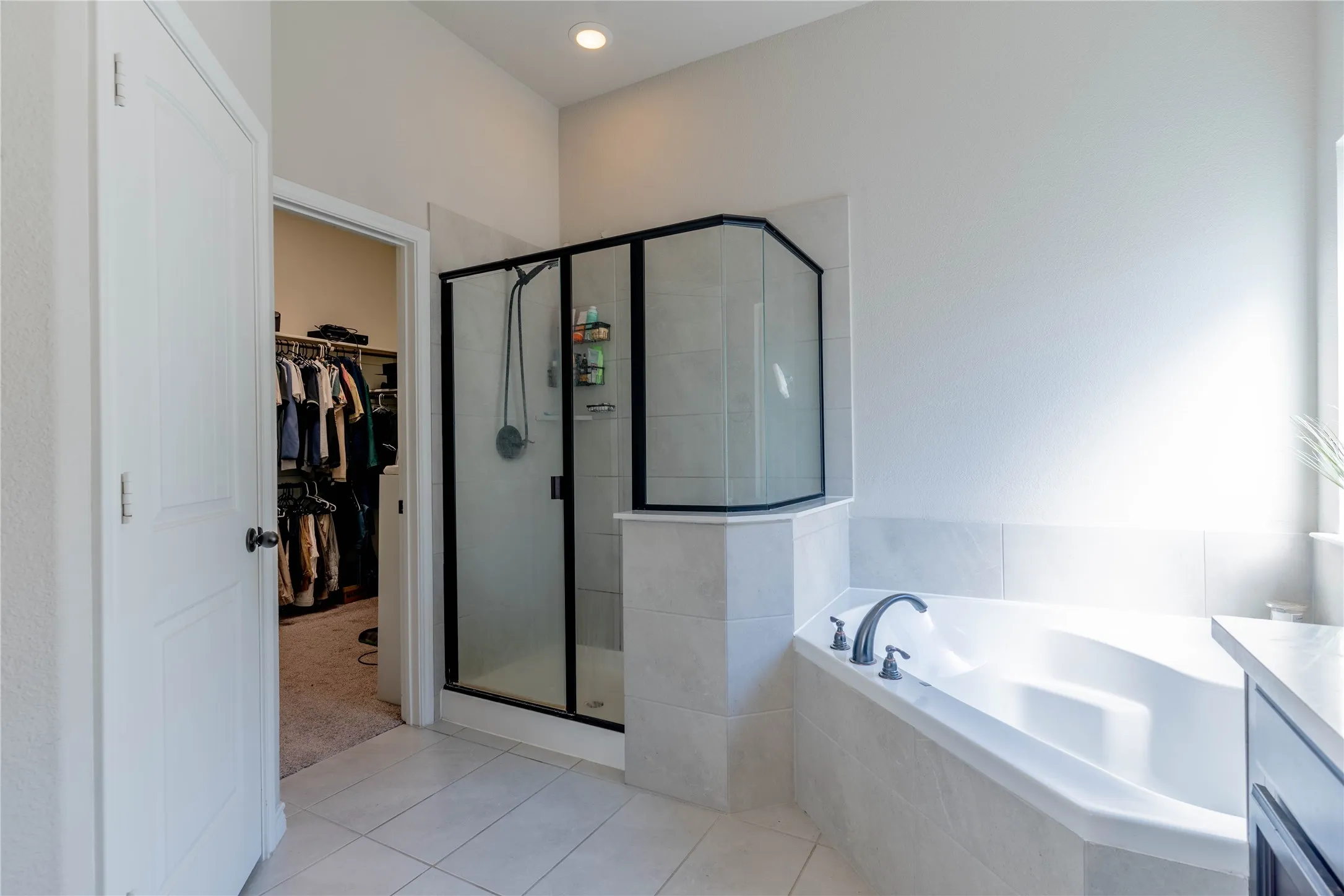Full bathroom featuring a spacious closet, a shower stall, a garden tub, vanity, and light tile patterned floors