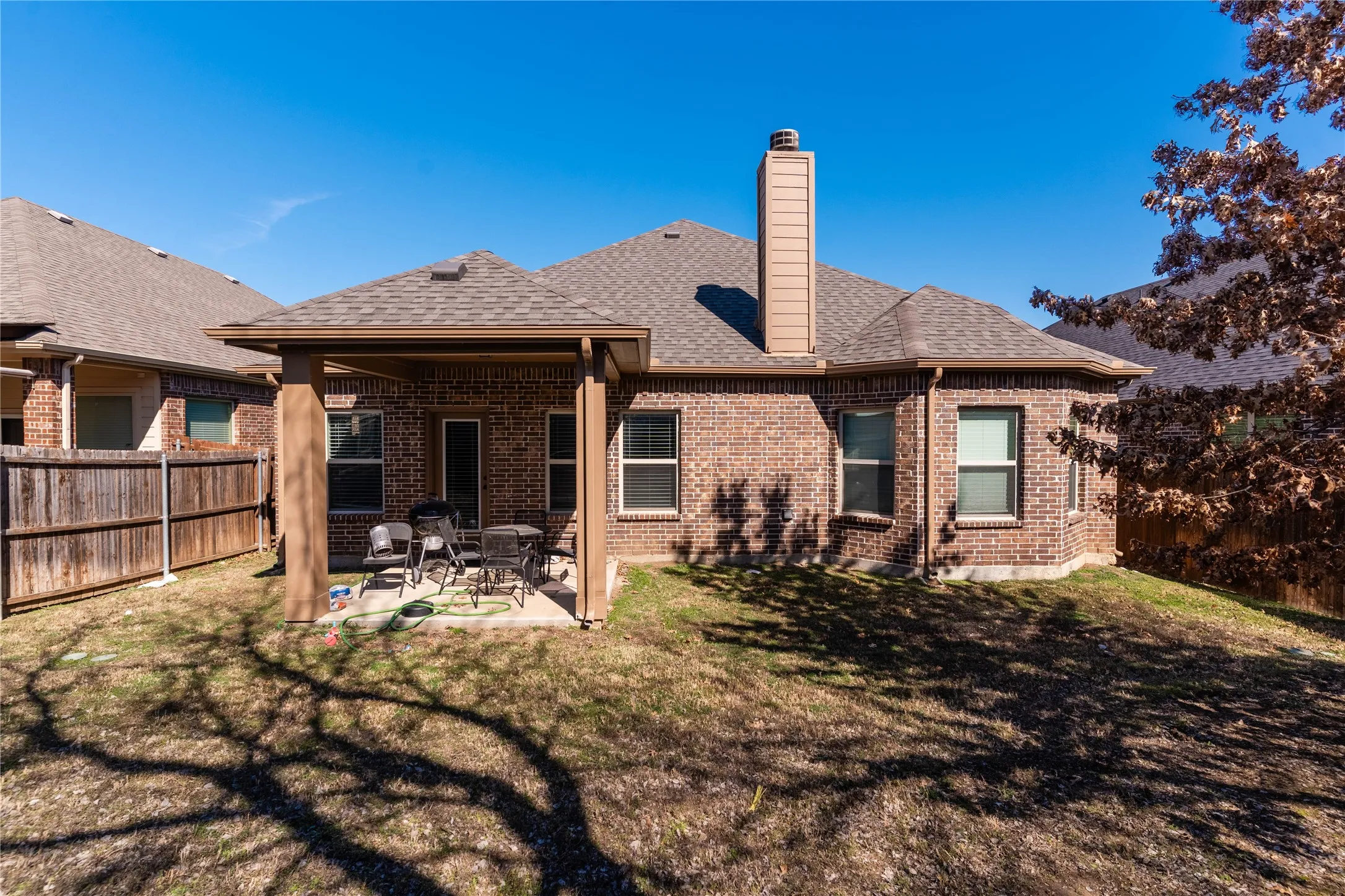 Rear view of house featuring a patio, a fenced backyard, brick siding, and a chimney