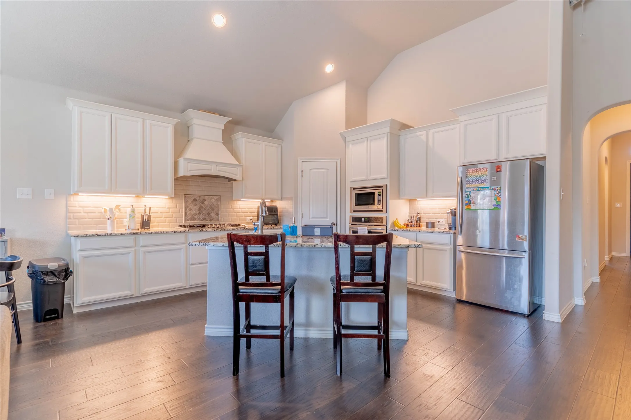 Kitchen with arched walkways, stainless steel appliances, white cabinets, backsplash, and light stone countertops