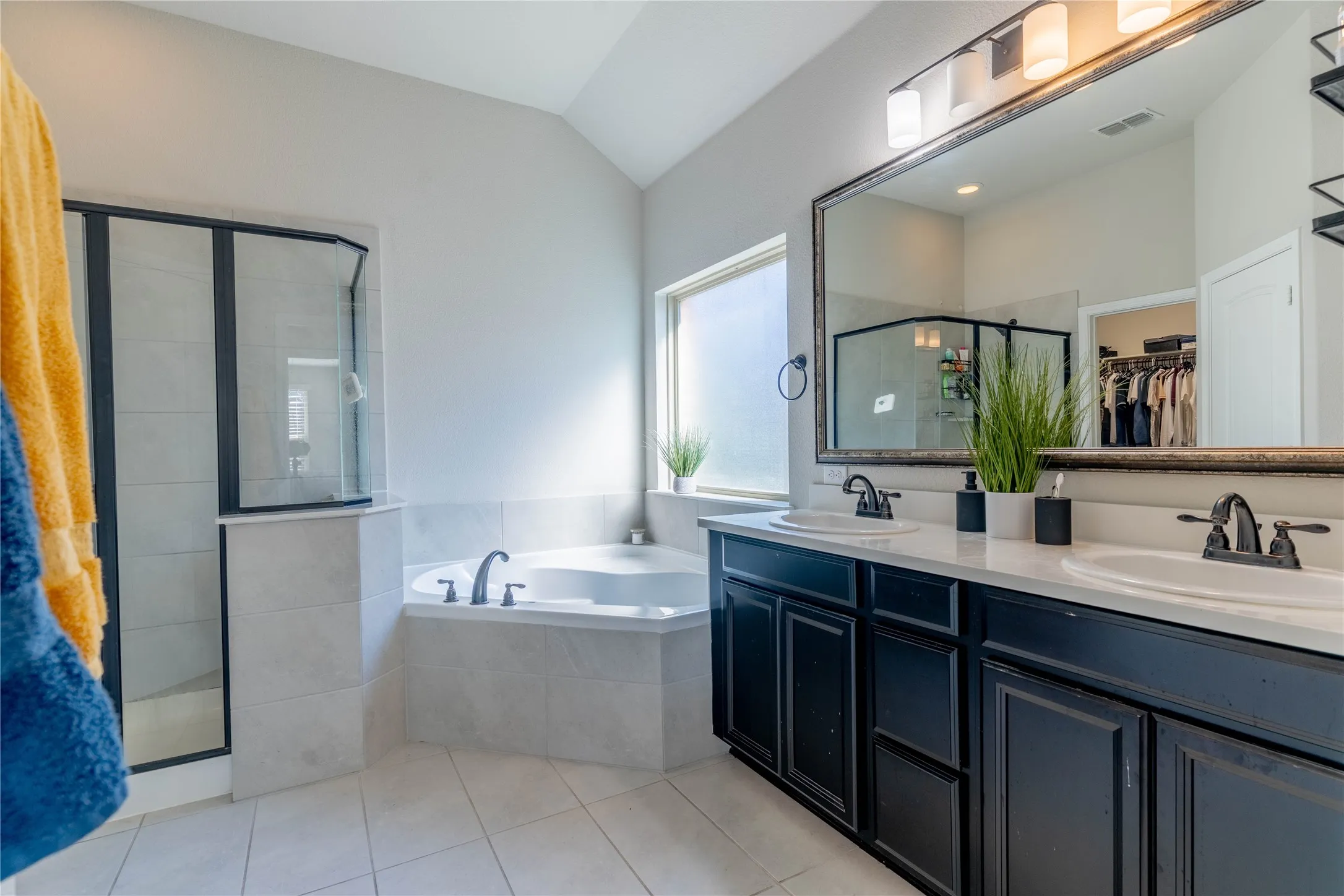 Full bathroom featuring a spacious closet, double vanity, a garden tub, a stall shower, and light tile patterned floors