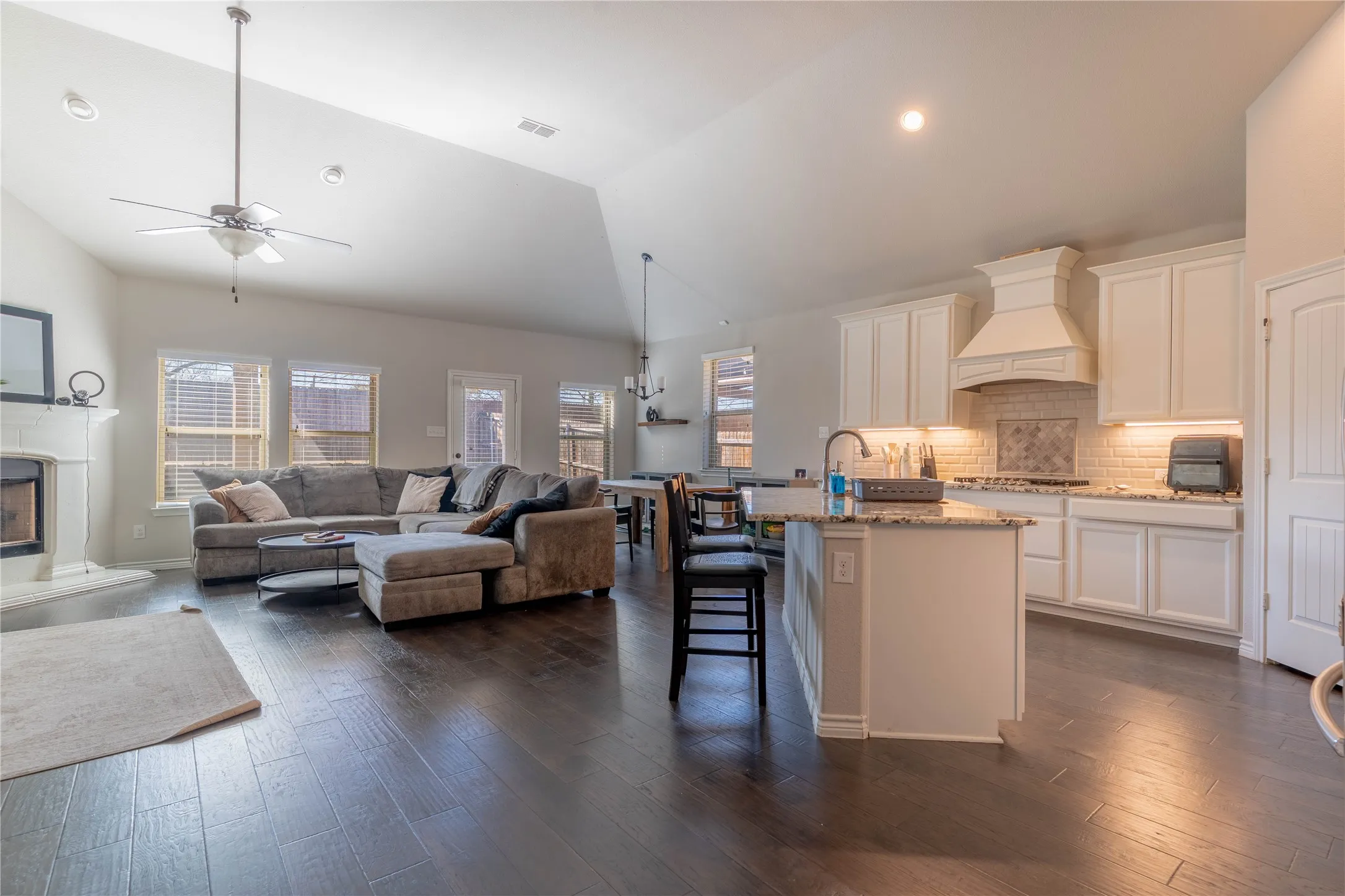 Kitchen featuring a breakfast bar area, open floor plan, white cabinetry, light stone countertops, and lofted ceiling