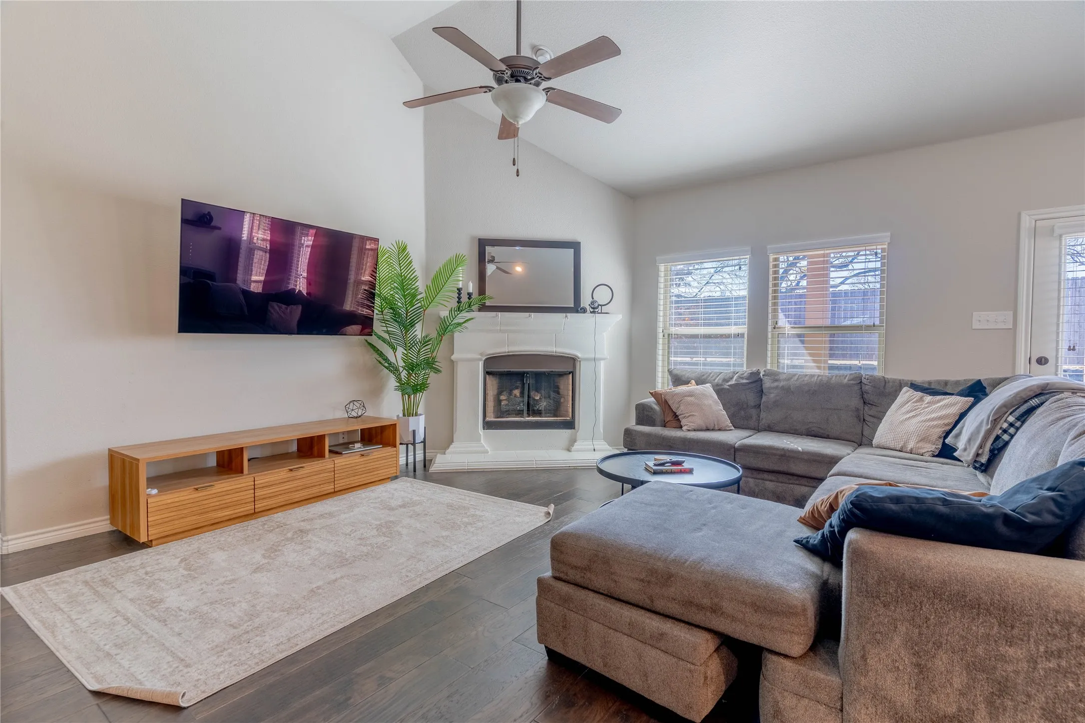 Living area with vaulted ceiling, ceiling fan, a fireplace with raised hearth, and dark wood-style floors