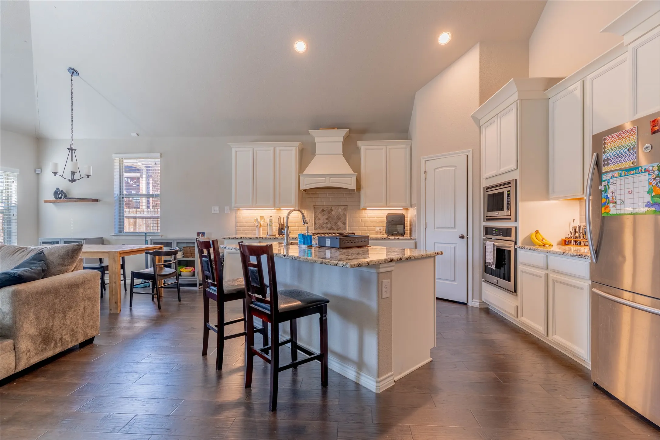 Kitchen with stainless steel appliances, light stone countertops, white cabinetry, a kitchen breakfast bar, and lofted ceiling