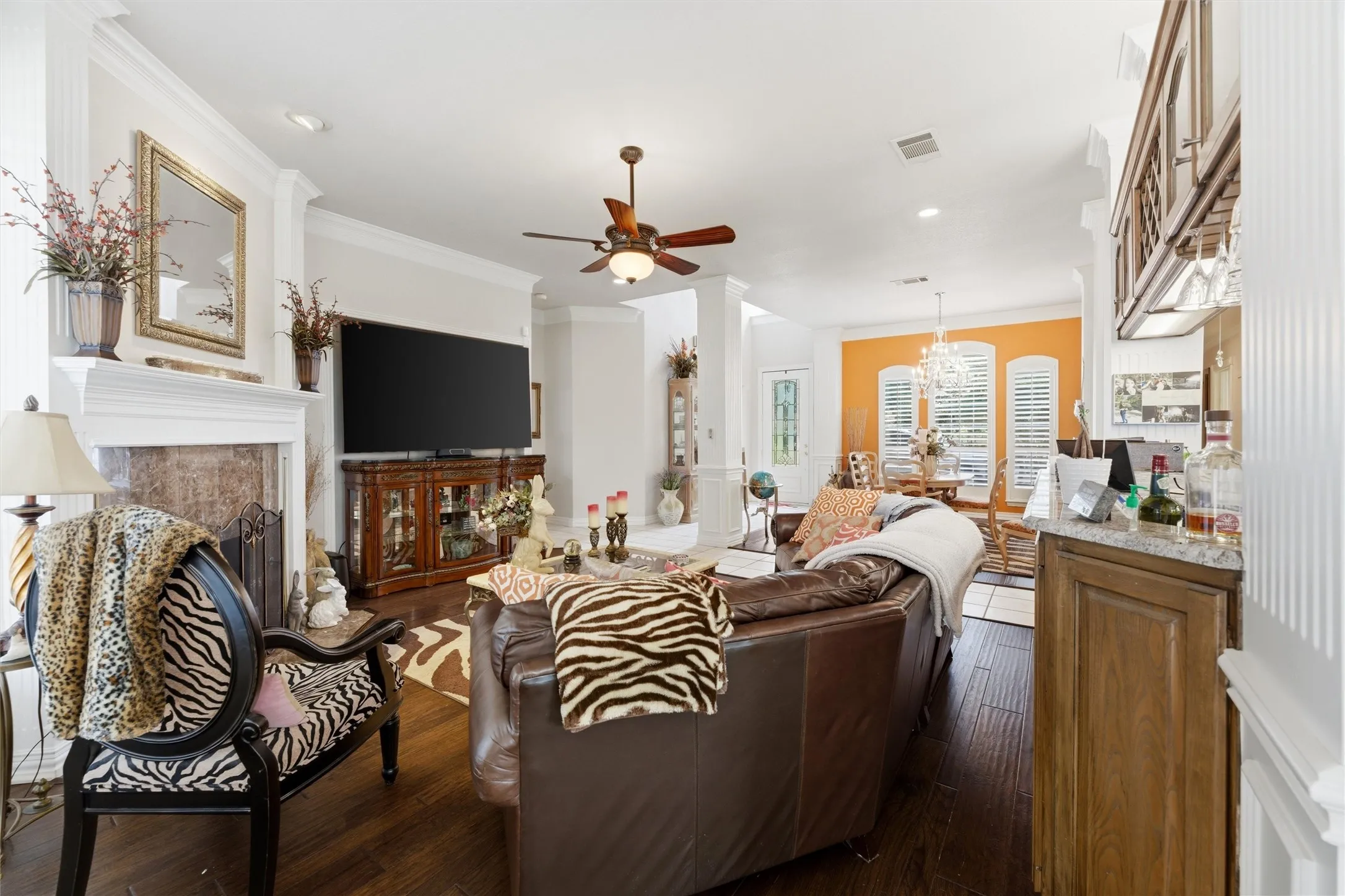 Living room featuring dark wood finished floors, crown molding, ceiling fan, a fireplace, and a chandelier