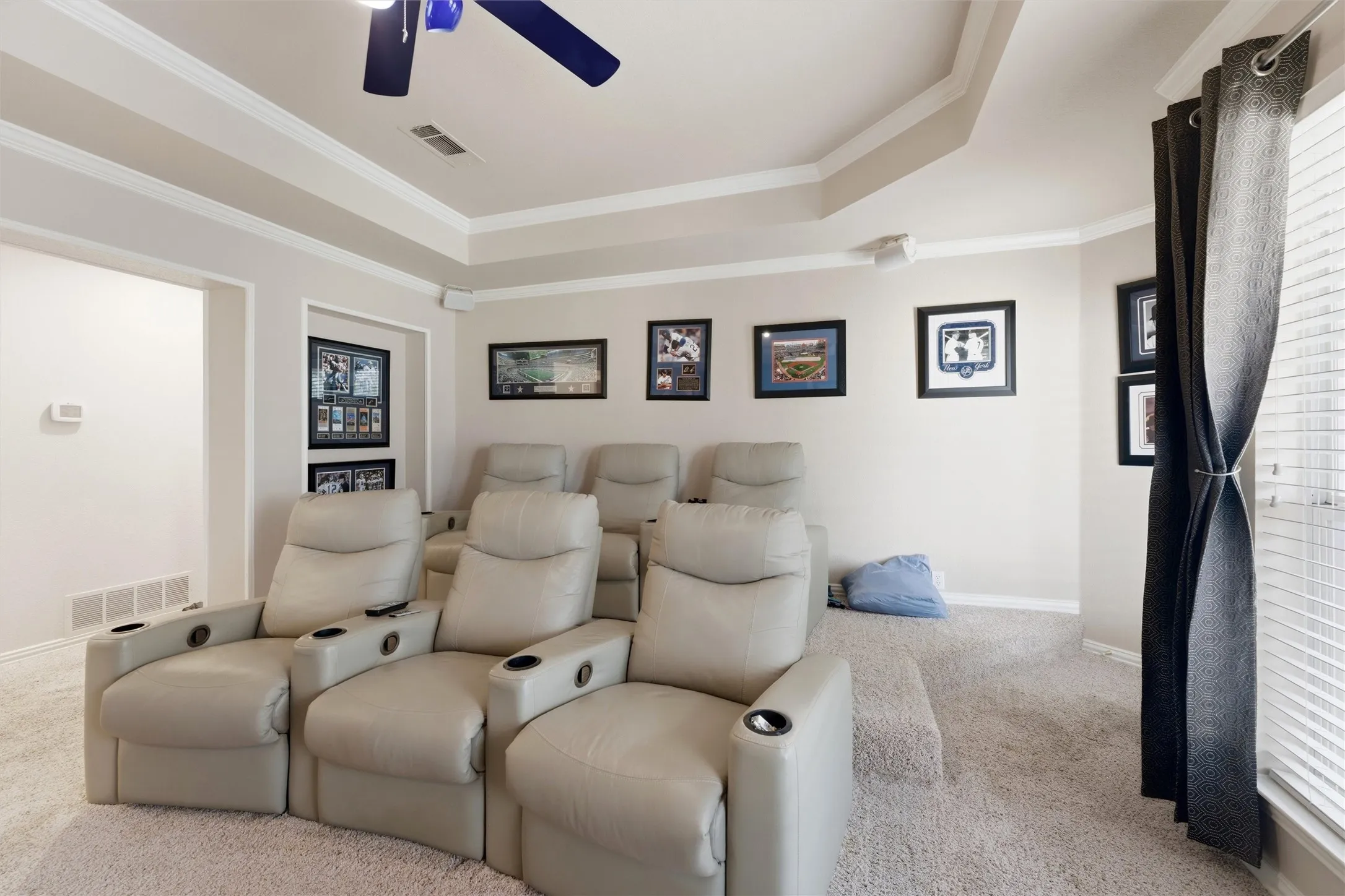Carpeted home theater with a raised ceiling, crown molding, and ceiling fan