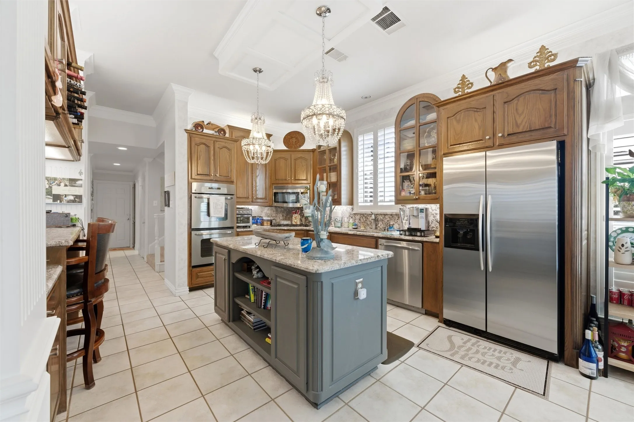 Kitchen featuring stainless steel appliances, a center island, light stone counters, light tile patterned floors, and crown molding