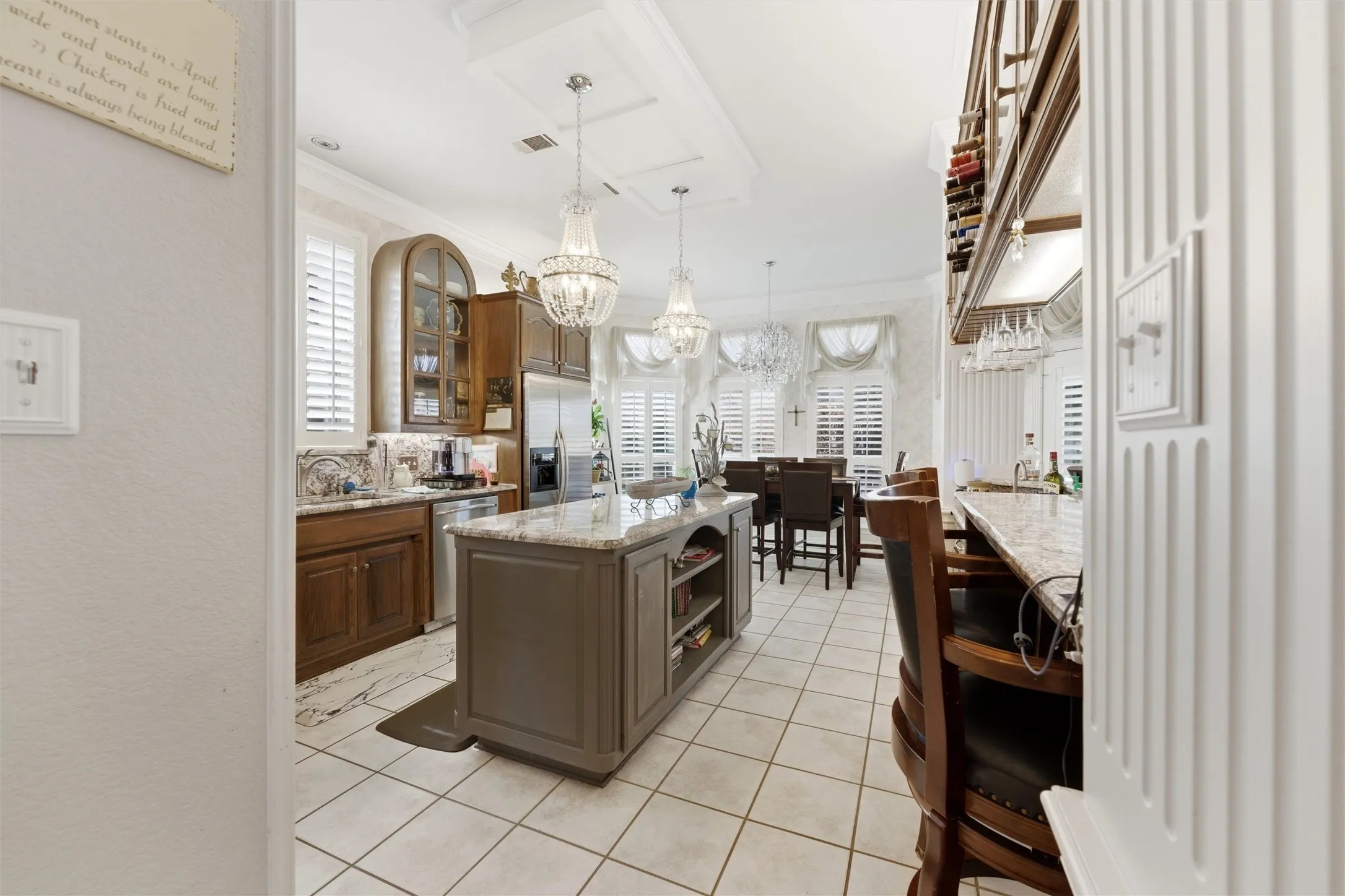 Kitchen with a kitchen island, glass fronted cabinets, light stone countertops, stainless steel appliances, and a chandelier