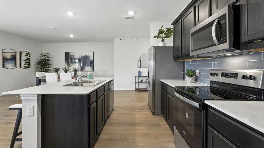 Kitchen featuring stainless steel appliances, a kitchen bar, an island with sink, light wood finished floors, and tasteful backsplash