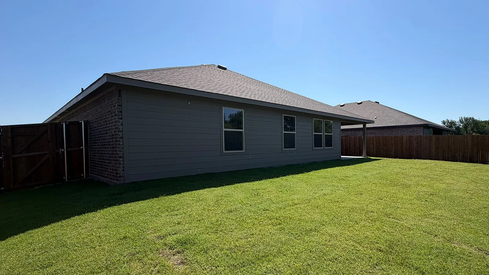 Expansive green lawn surrounds the property, featuring a privacy fence and a covered patio area