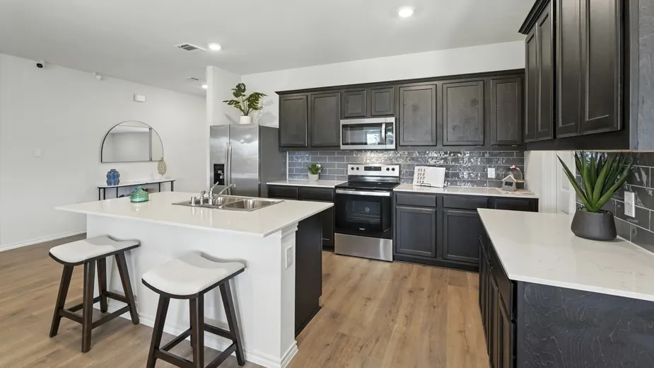 Kitchen featuring stainless steel appliances, an island with sink, a breakfast bar, backsplash, and light wood-type flooring