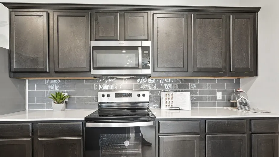 Kitchen featuring stainless steel appliances, decorative backsplash, dark wood finish cabinets, and light stone counters