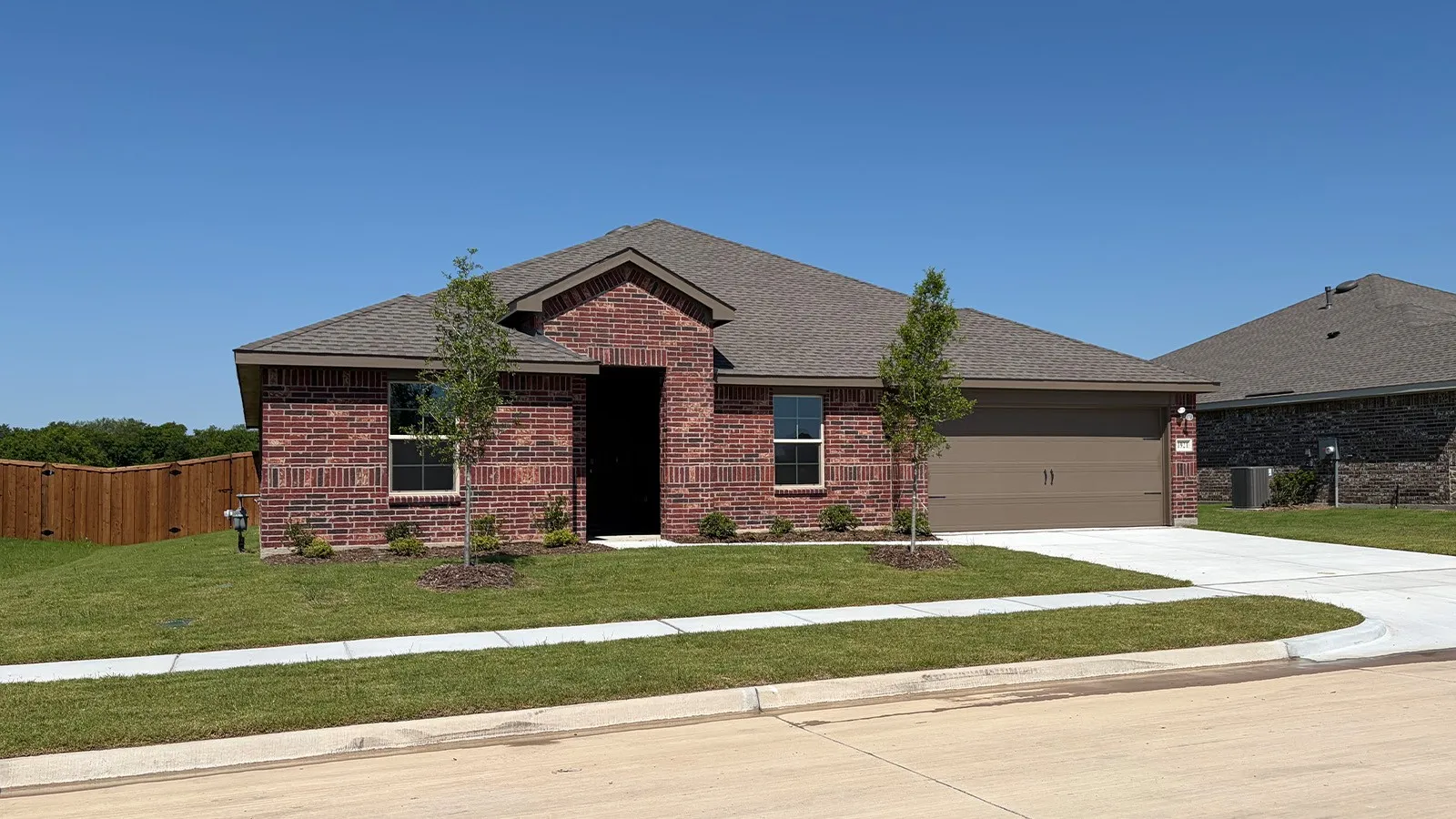 Brick exterior with a peaked roofline, an attached two-car garage, a concrete driveway, a manicured lawn, and a privacy fence along the property line