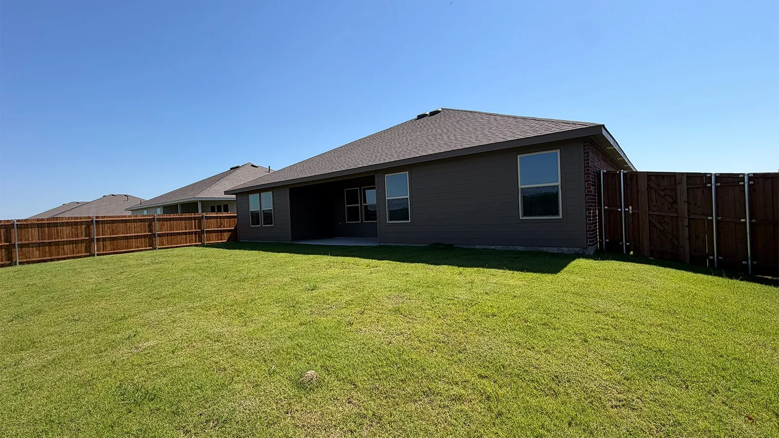Expansive backyard featuring a lush lawn, privacy fencing, a covered patio, and a shingled roofline