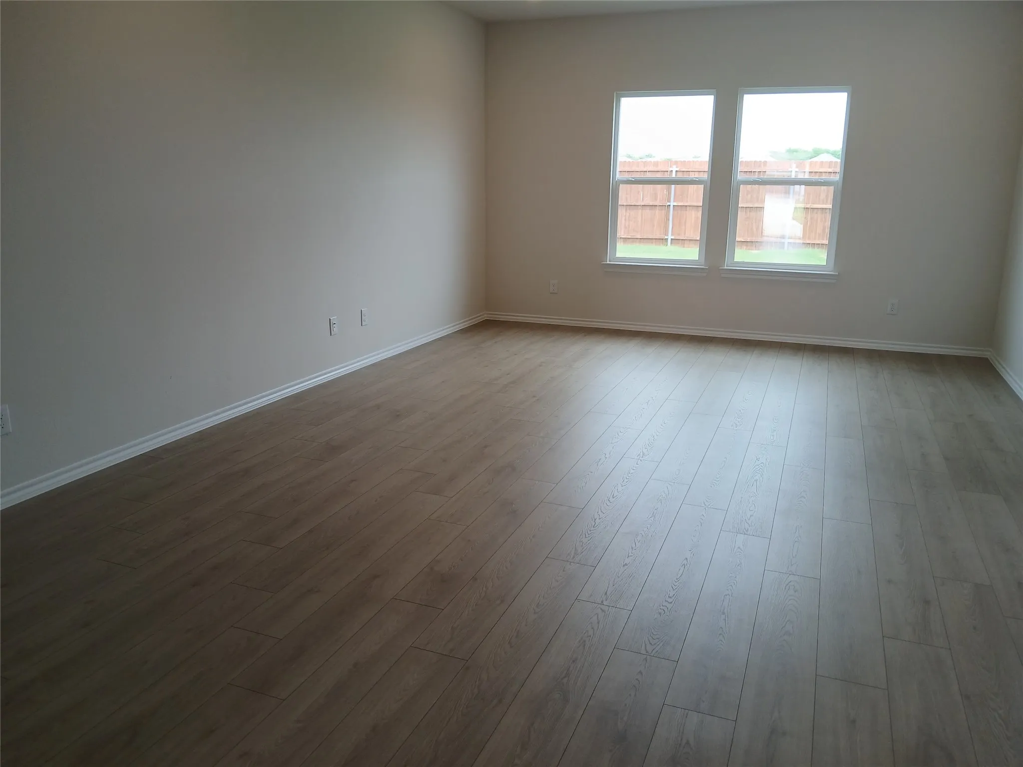 Spacious room featuring wood-finish flooring, light-toned walls, and white trim