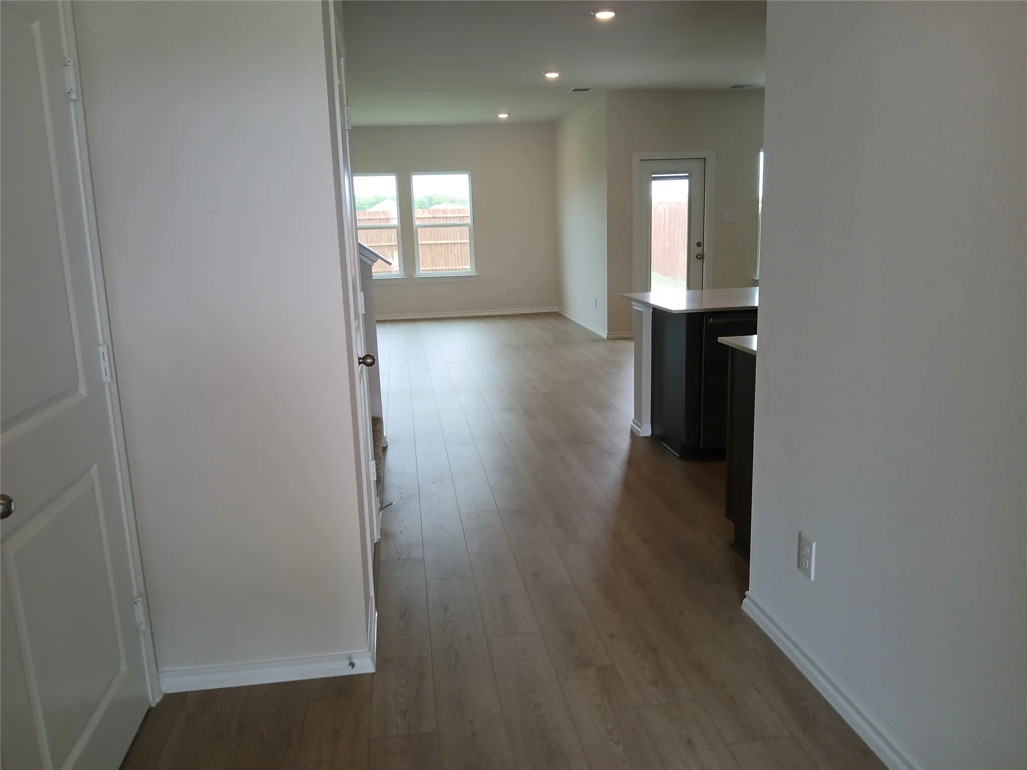 Open concept living area featuring wood-finish flooring, recessed lighting, double windows, and a rear exterior door