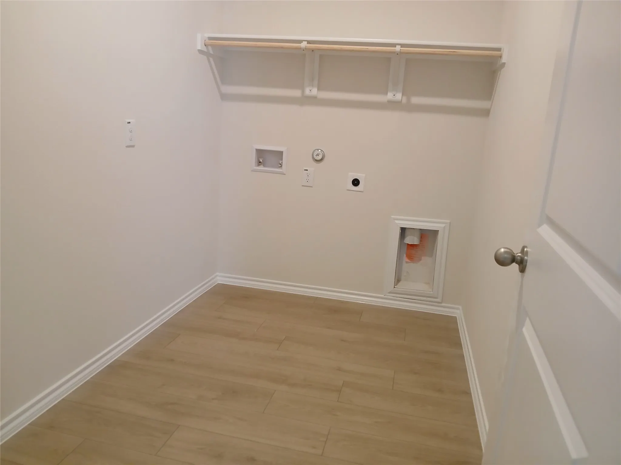 Dedicated laundry area featuring a wood-finish floor, white baseboards, and a built-in shelf with a hanging rod