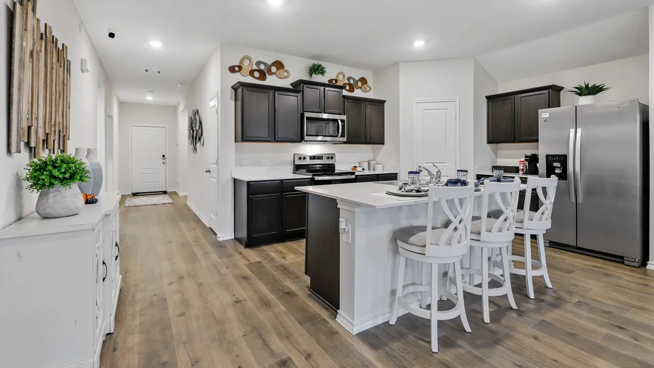 Open-concept kitchen featuring dark wood cabinetry, light countertops, a central island with a sink, stainless steel appliances, and wood-finish flooring throughout