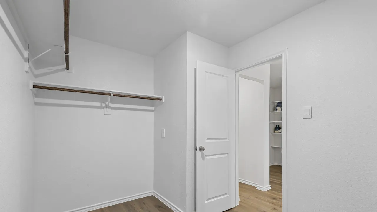 Walk-in closet with wood-finish flooring, white walls, and built-in shelving