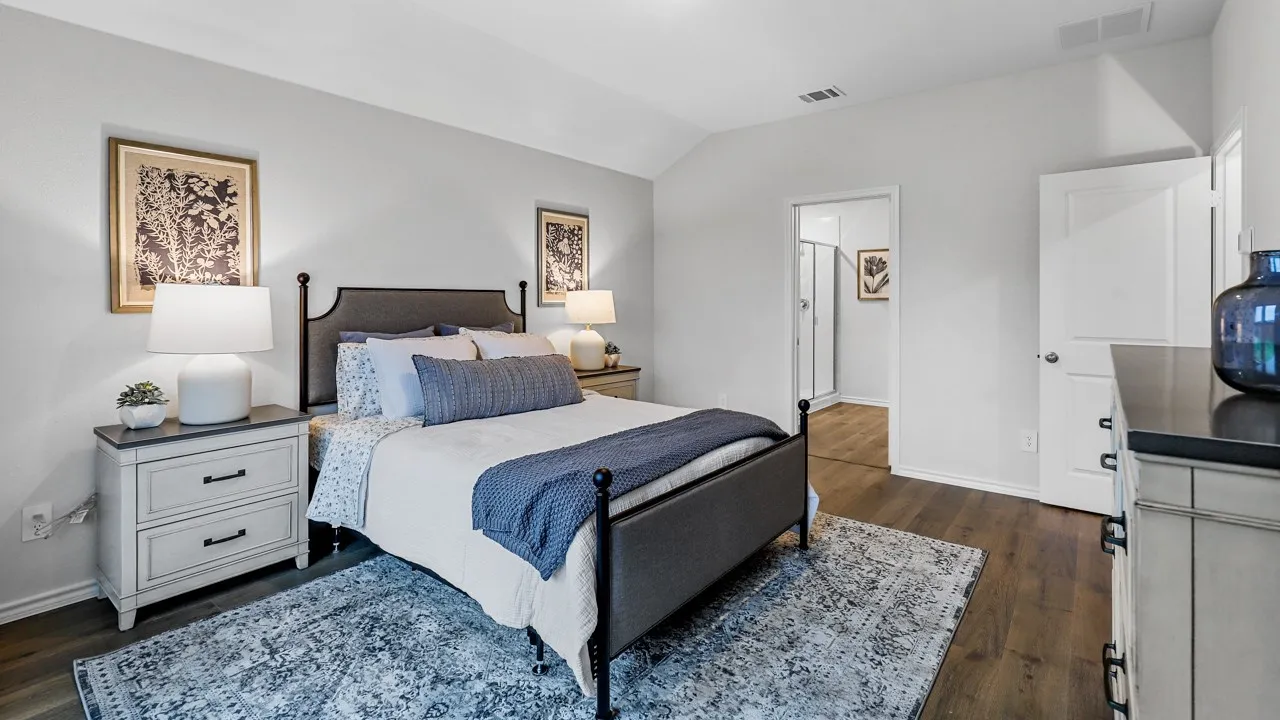 Spacious sleeping area featuring vaulted ceilings, wood-finish flooring, light gray walls, and a recessed doorway providing access to an adjacent bathroom with a glass-enclosed shower