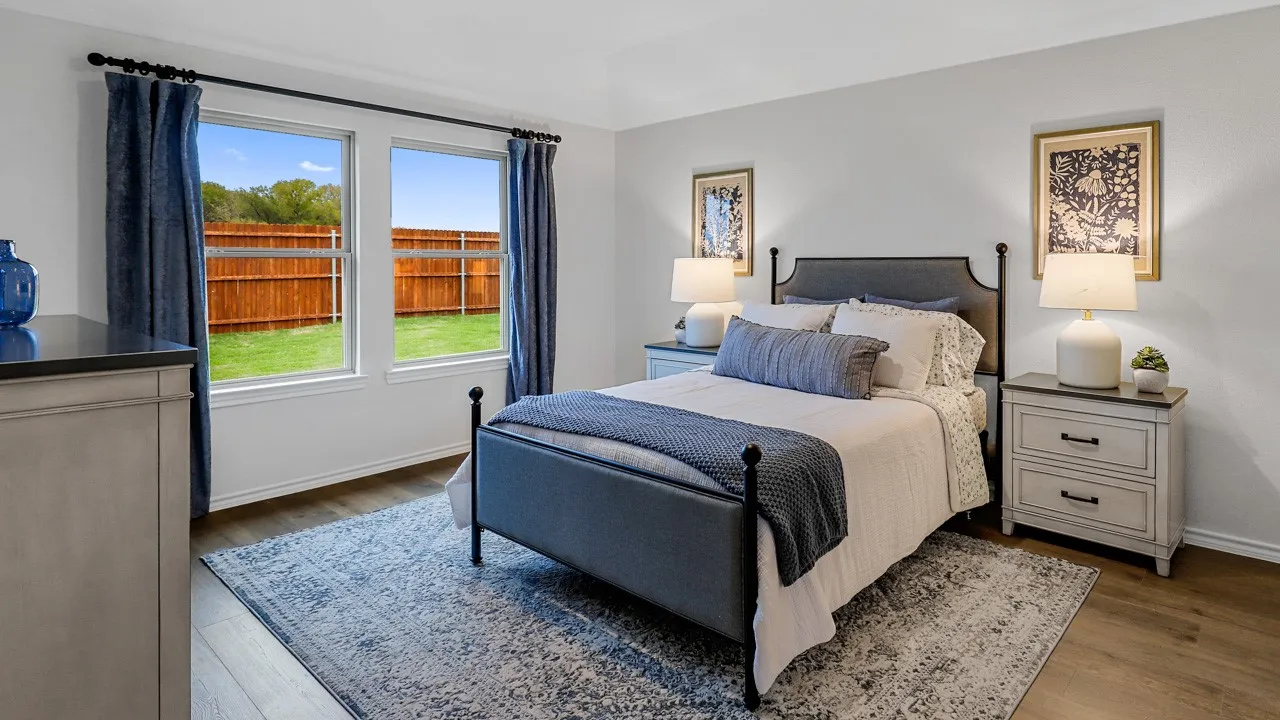 Bedroom featuring wood-finish flooring, two large windows, a fenced backyard, and a high ceiling
