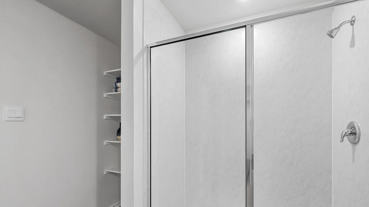 Shower enclosure with sliding glass doors, white shower walls, and a chrome shower head and faucet