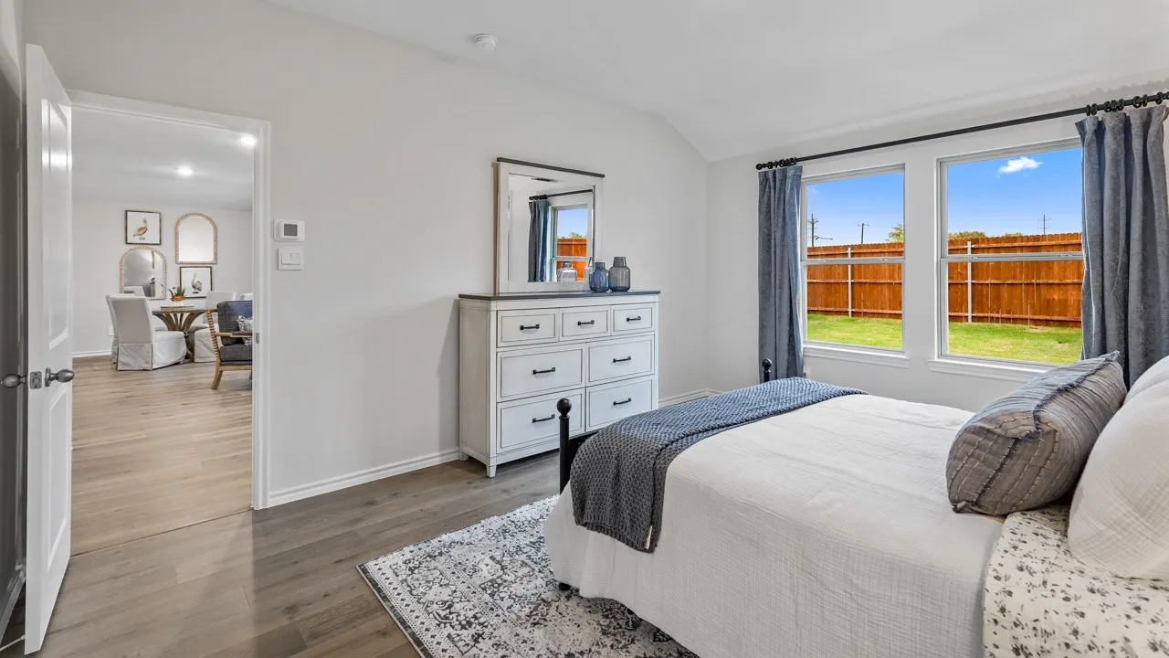 Spacious room featuring wood-finish flooring, white walls, and a pair of large windows overlooking a fenced backyard