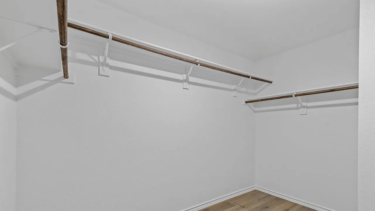 Spacious walk-in closet featuring light wood-finish flooring and multiple shelving units with integrated hanging rods
