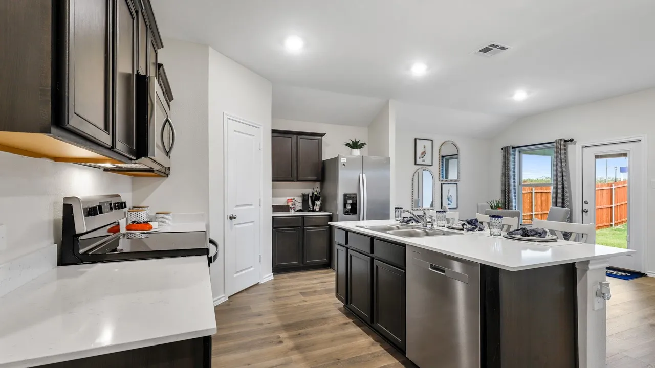 Open-concept kitchen featuring dark cabinetry, white countertops, wood-finish flooring, stainless steel appliances, and an island with an integrated sink