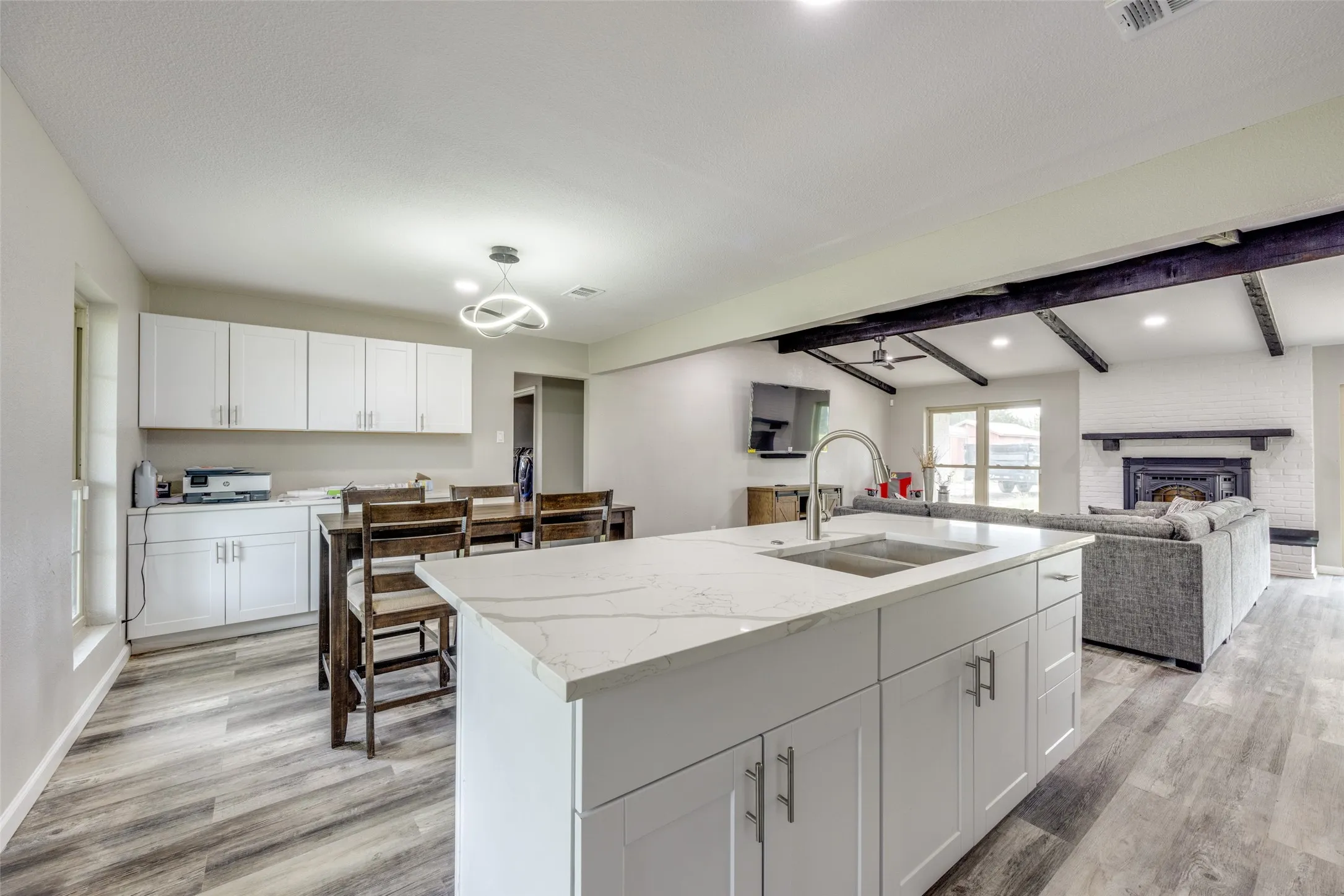 Kitchen featuring light wood finished floors, white cabinetry, open floor plan, light stone counters, and beam ceiling