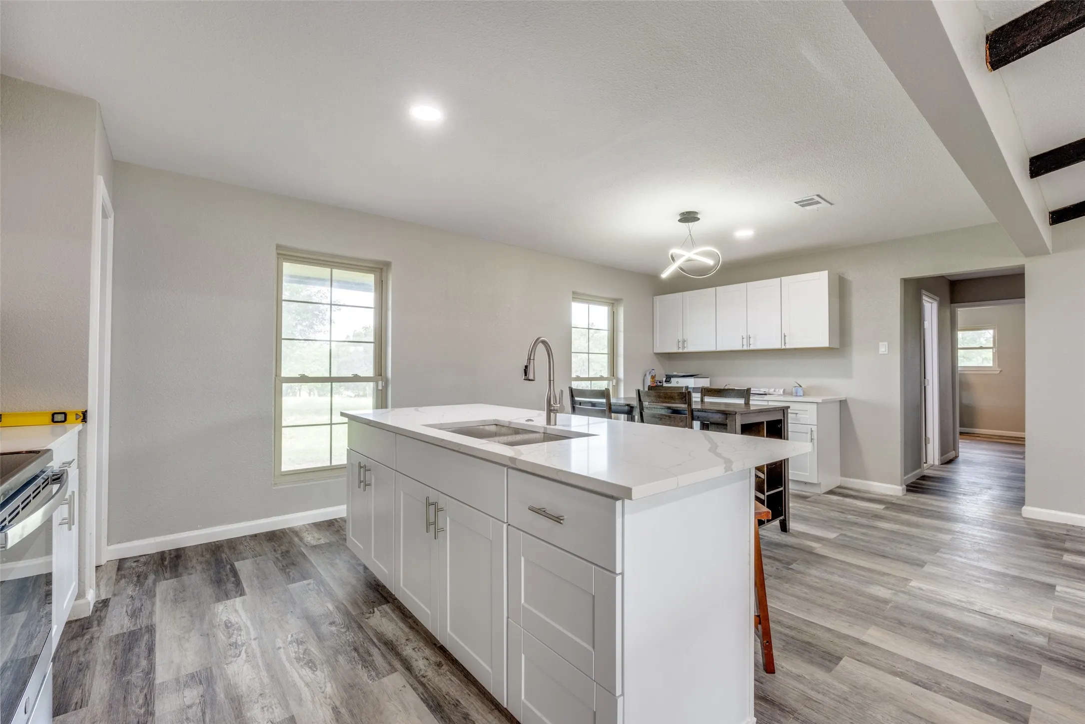 Kitchen with a chandelier, light wood-type flooring, white cabinetry, a center island with sink, and recessed lighting