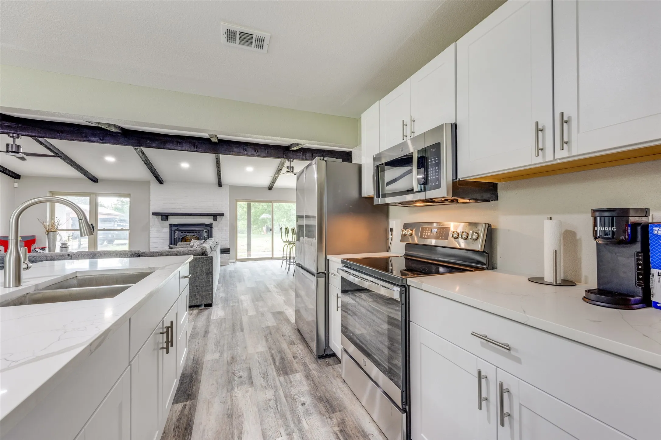 Kitchen featuring appliances with stainless steel finishes, light wood-style floors, white cabinets, beamed ceiling, and light stone countertops