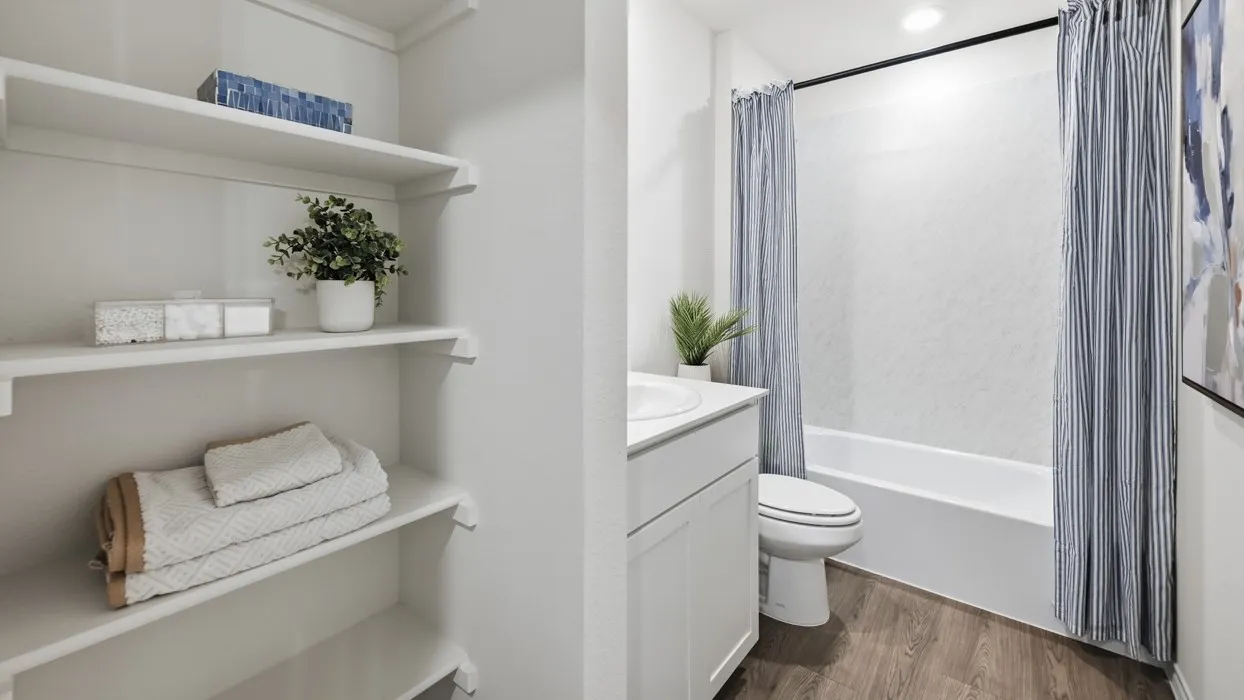 Bathroom featuring a white vanity with integrated sink, toilet, and a bathtub with a textured surround