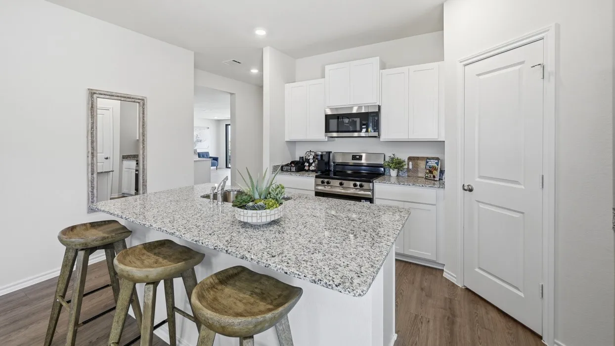 Kitchen featuring a large island with a stainless steel sink, granite-style countertops, white cabinetry, and wood-finish flooring