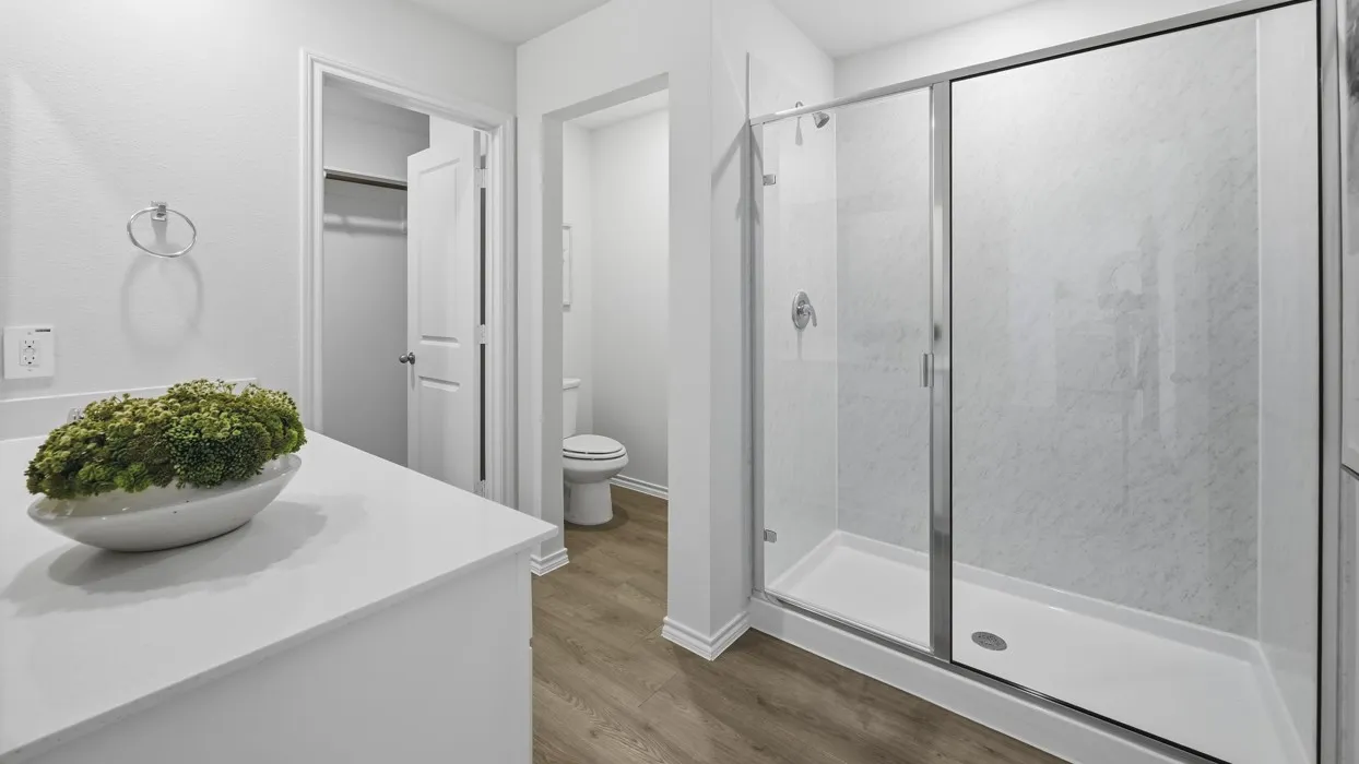 White countertop vanity with a chrome towel ring, glass-enclosed shower, and wood-finish flooring