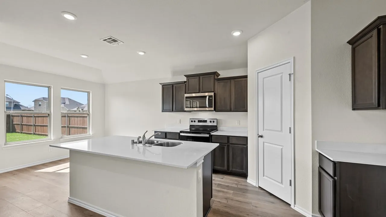 Open-concept kitchen featuring dark wood cabinetry, white countertops, stainless steel appliances, a center island with an undermount sink, and recessed lighting