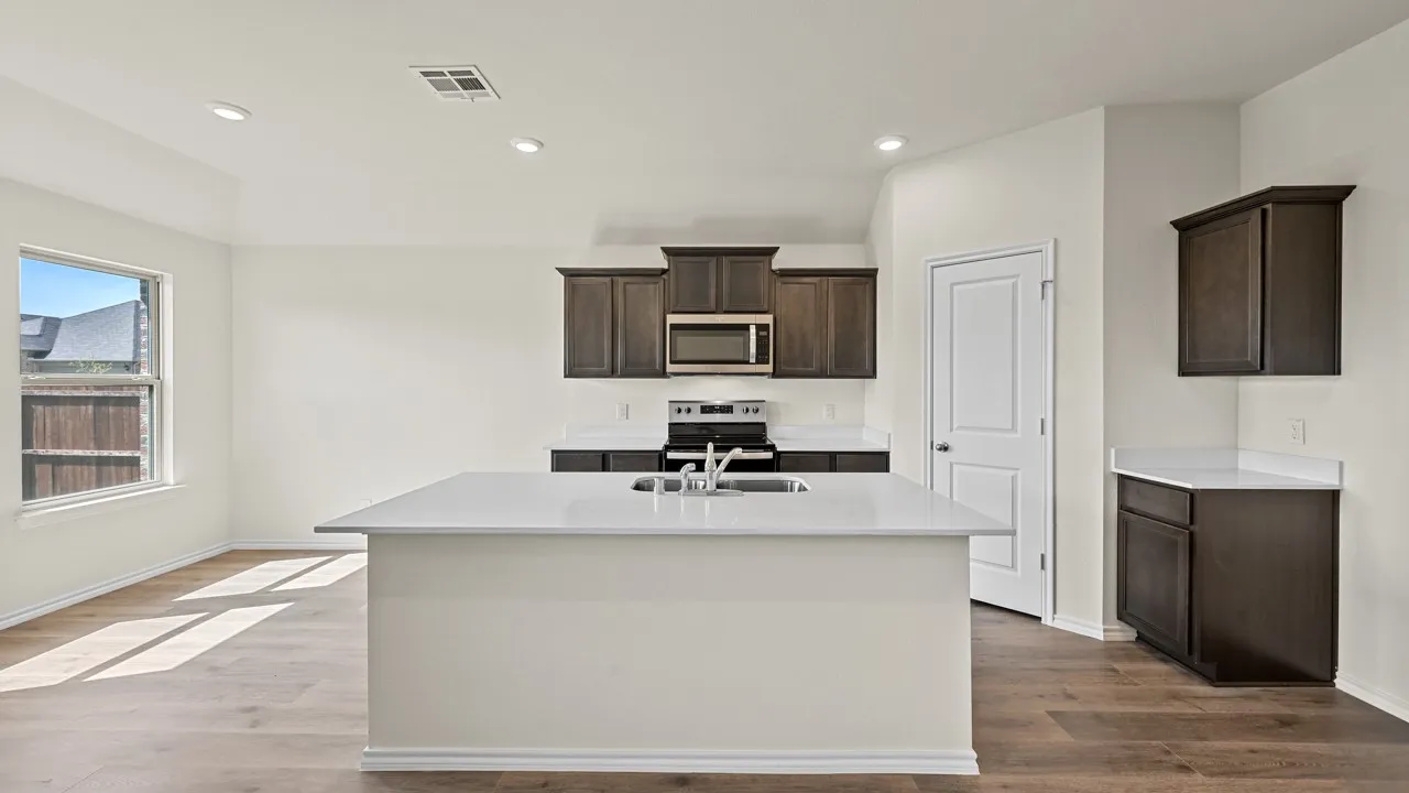 Open-concept kitchen featuring a central island with an undermount sink, dark wood-finish cabinetry, stainless steel appliances, and light-toned countertops