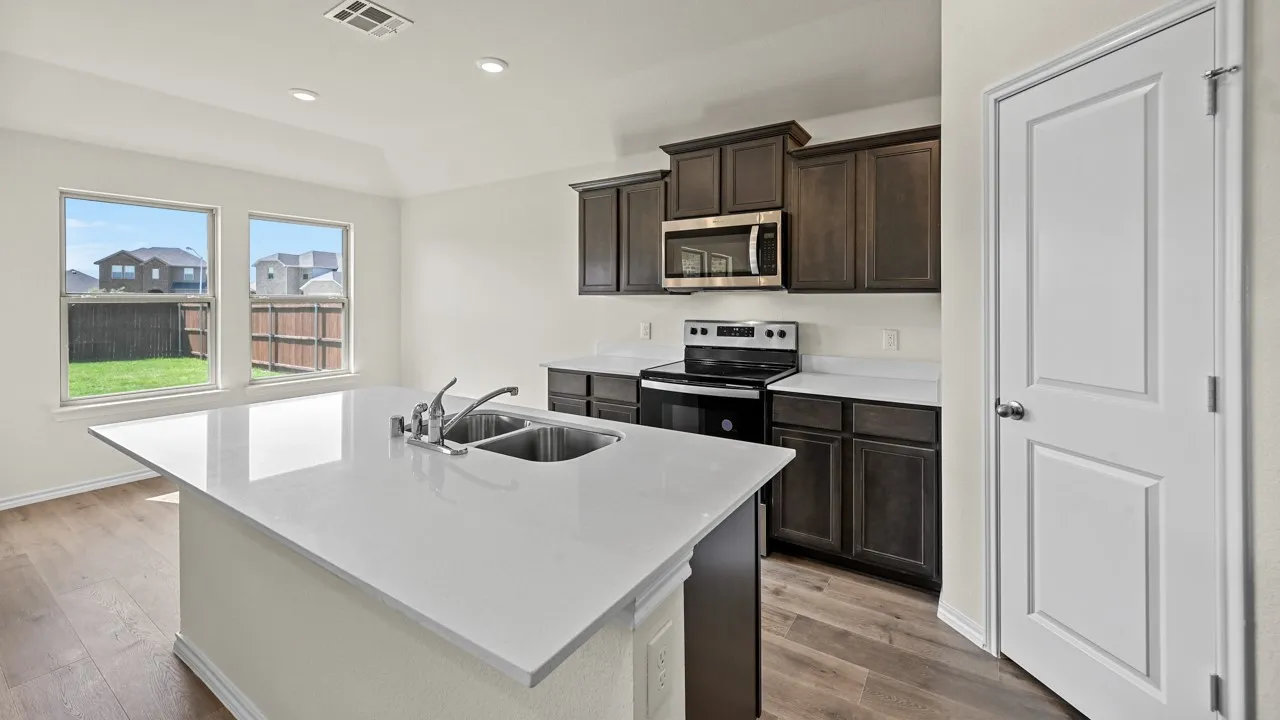 Kitchen featuring a large central island with a double basin sink, white countertops, dark wood-finish cabinetry, stainless steel microwave, and wood-finish flooring