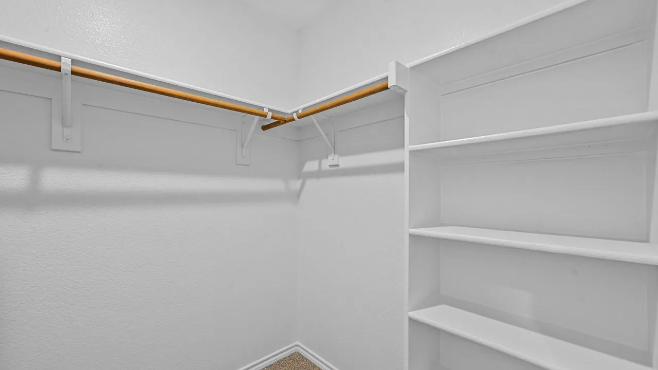 Walk-in closet with built-in shelving, two wood-finish hanging rods, and light-toned carpet flooring