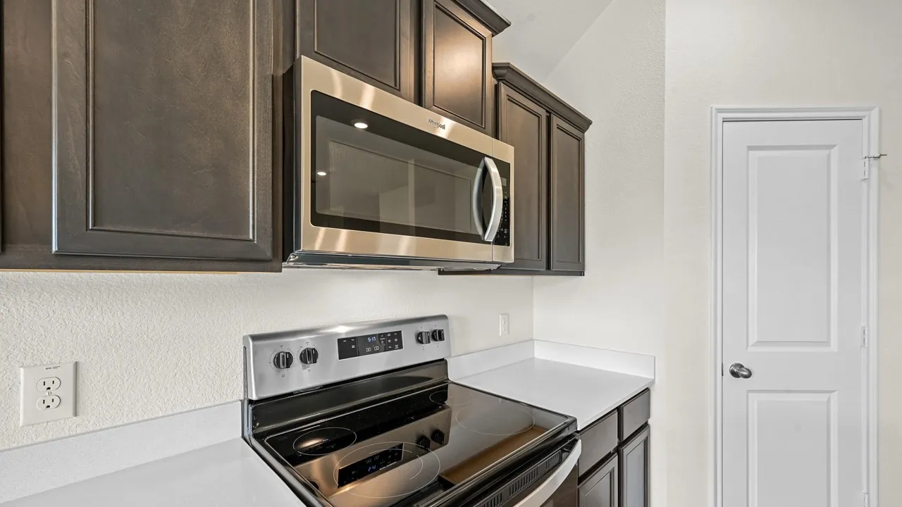 Modern kitchen featuring stainless steel appliances, dark wood cabinetry, and white countertops