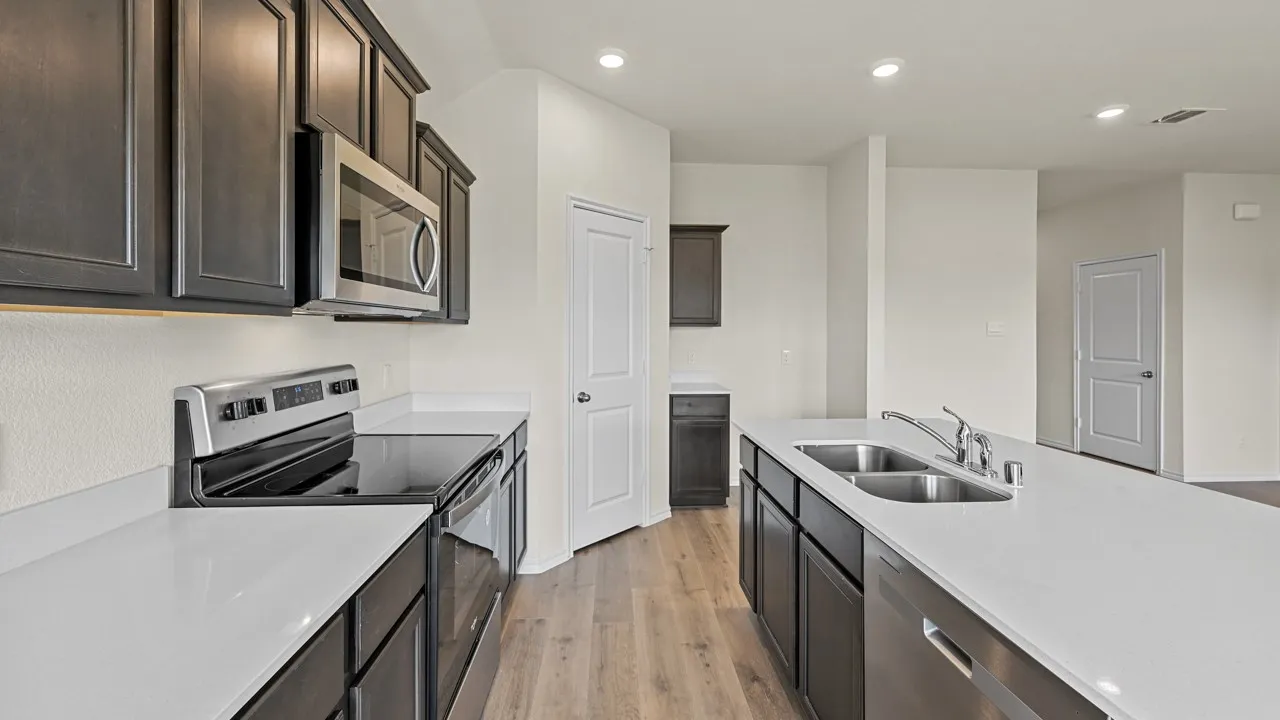 Kitchen featuring a large island with a double basin sink, stainless steel appliances, dark wood-finish cabinetry, and light-tone countertops