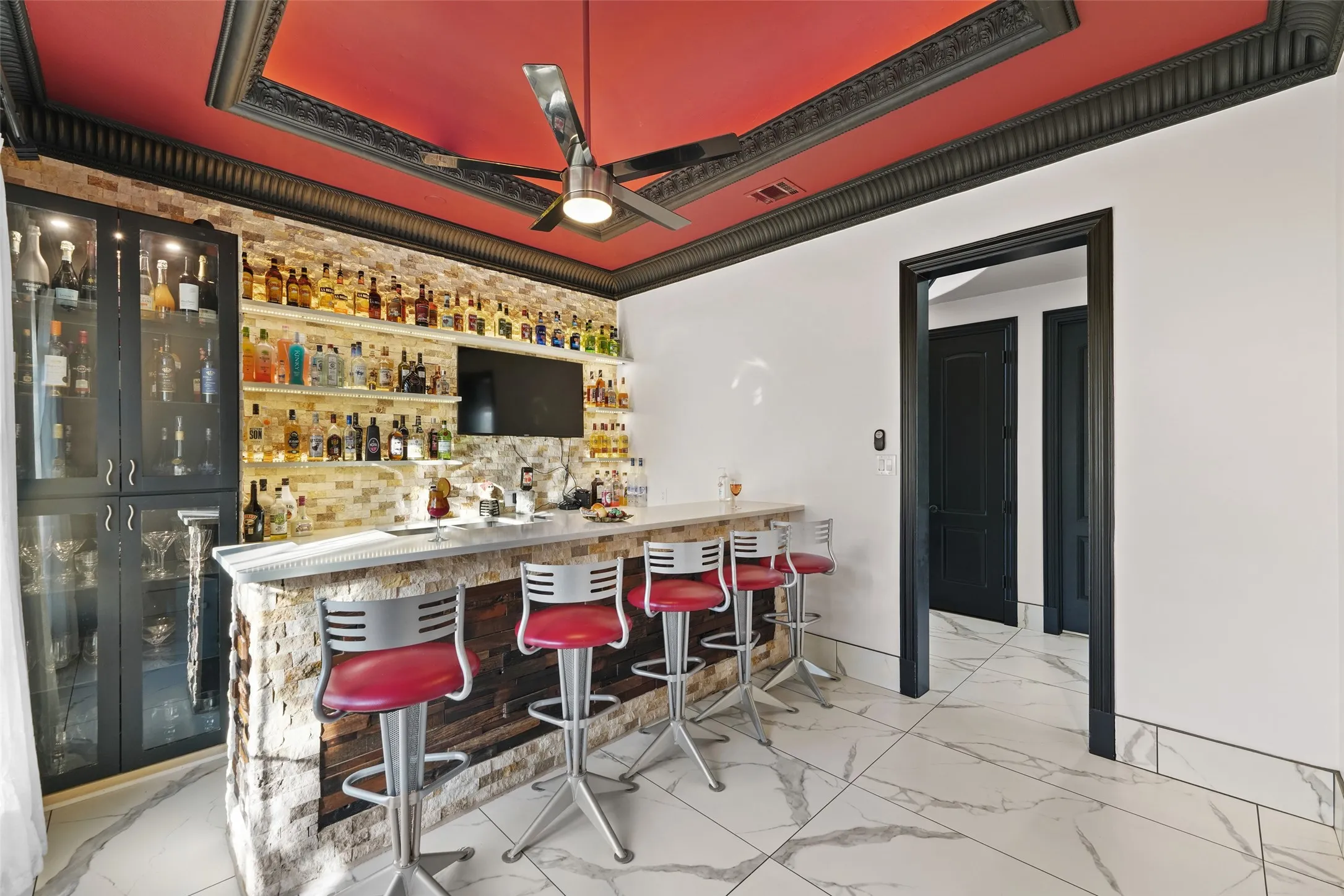 Indoor bar featuring open shelves, light marble finish flooring, ceiling fan, and glass insert cabinets