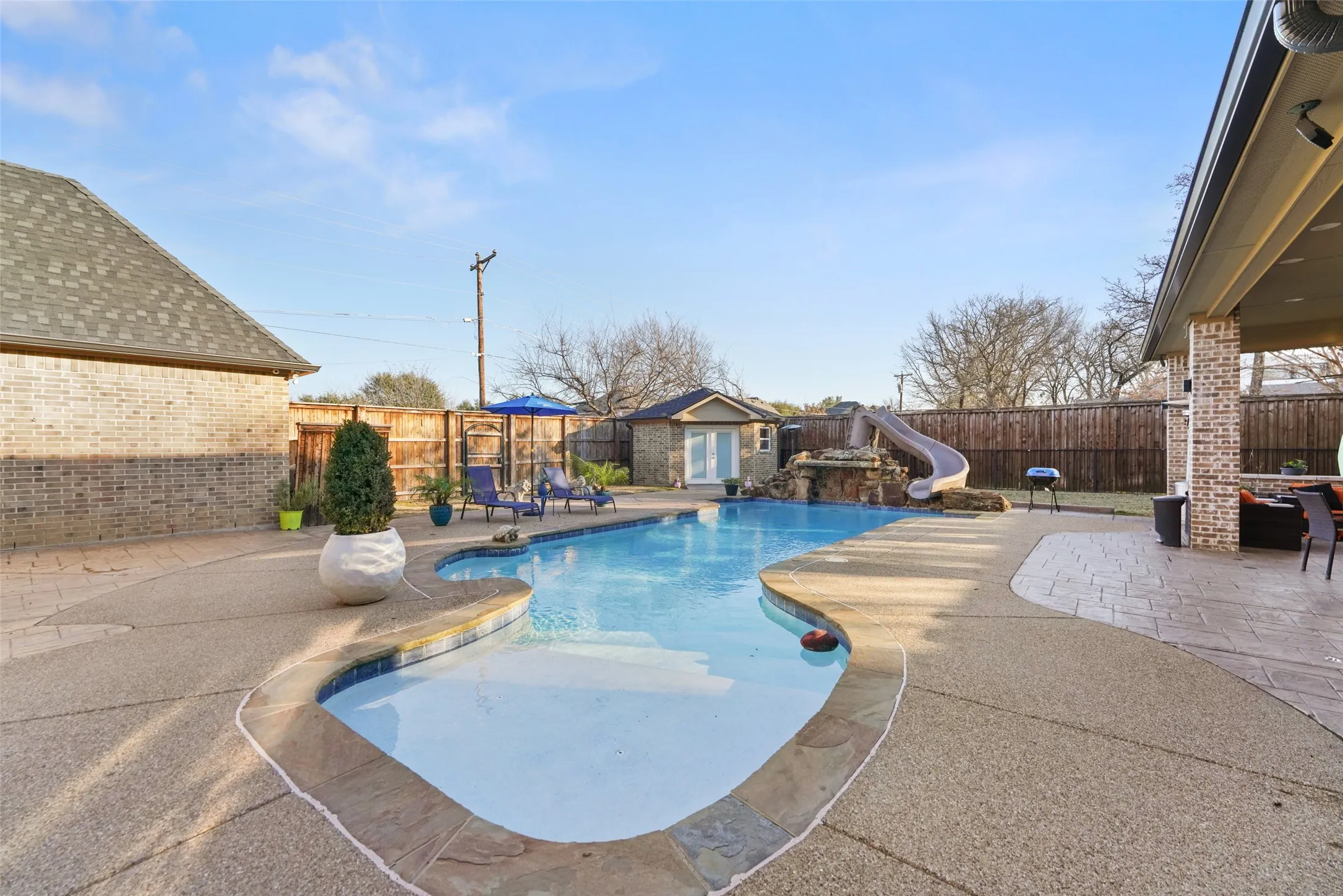View of pool featuring patio surround, a water slide, an outdoor structure, and a fenced backyard