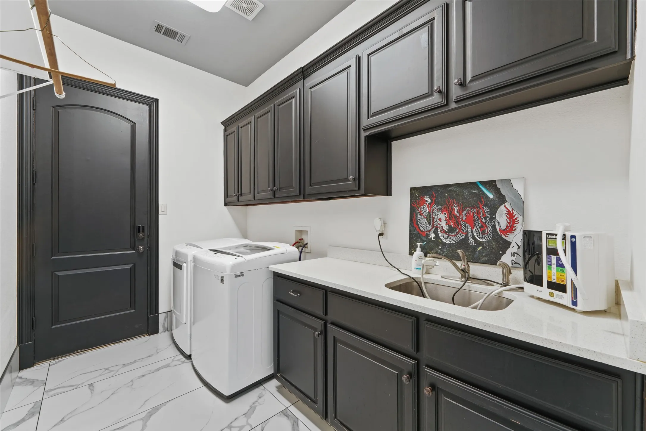 Laundry area featuring light marble finish floors, washing machine and clothes dryer, and cabinet space