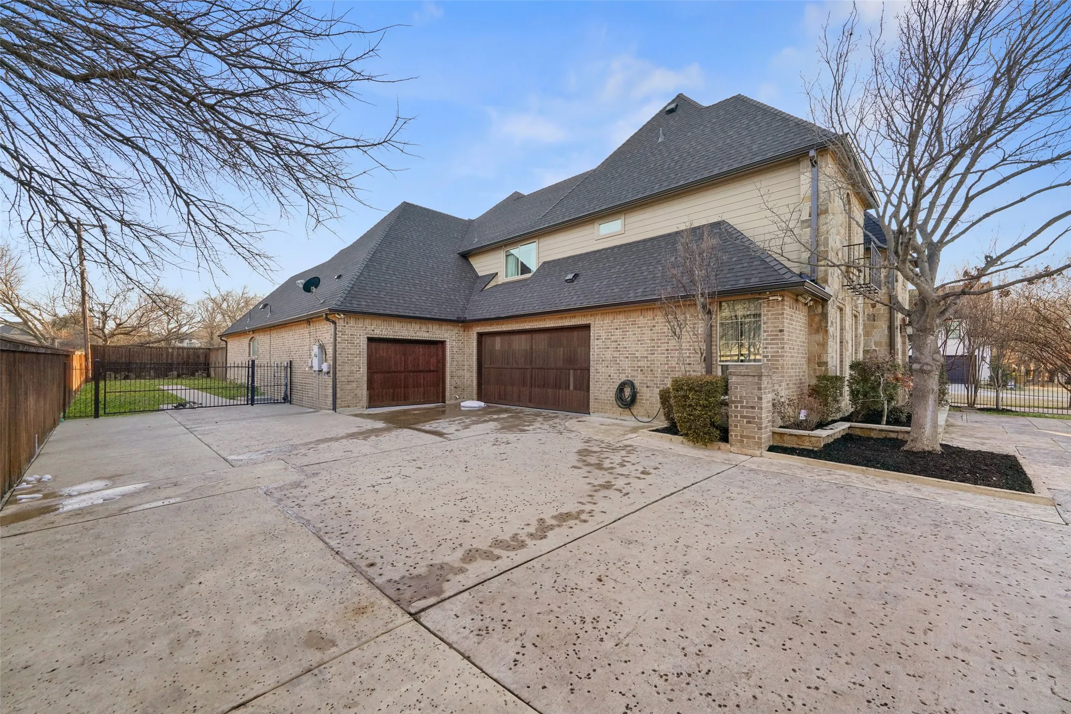 View of side of home with driveway, a gate, brick siding, a shingled roof, and an attached garage